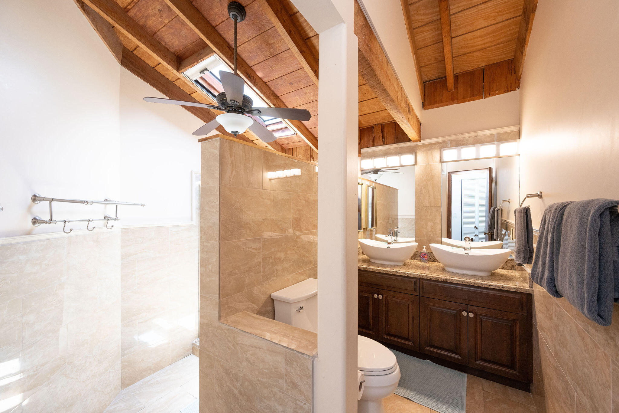 Bathroom with a tiled walk-in shower, double vessel sinks, and a vaulted wood-beam ceiling with skylights.