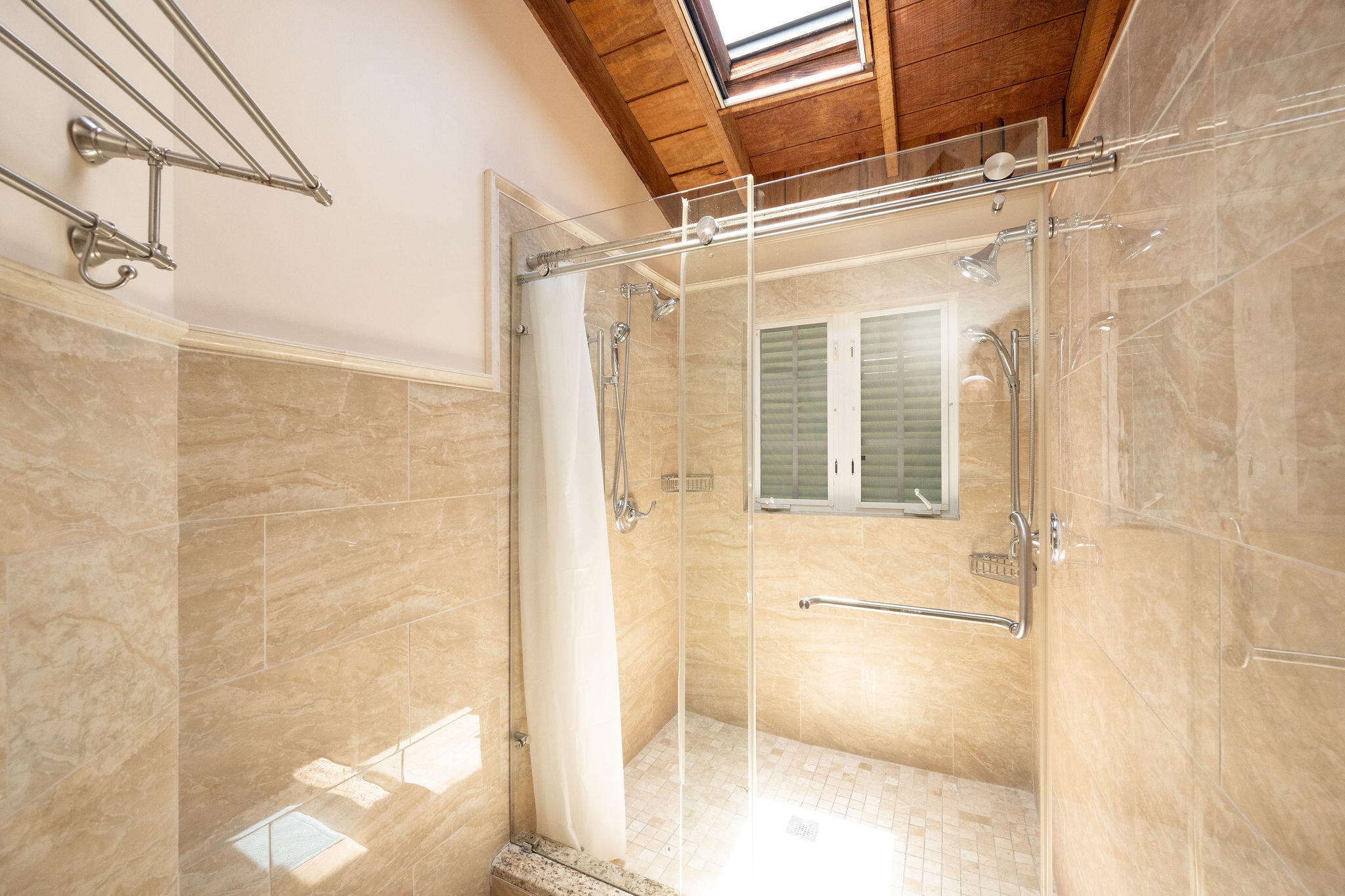 Bathroom with a glass-enclosed tiled shower beneath a skylight and vaulted wood ceiling.