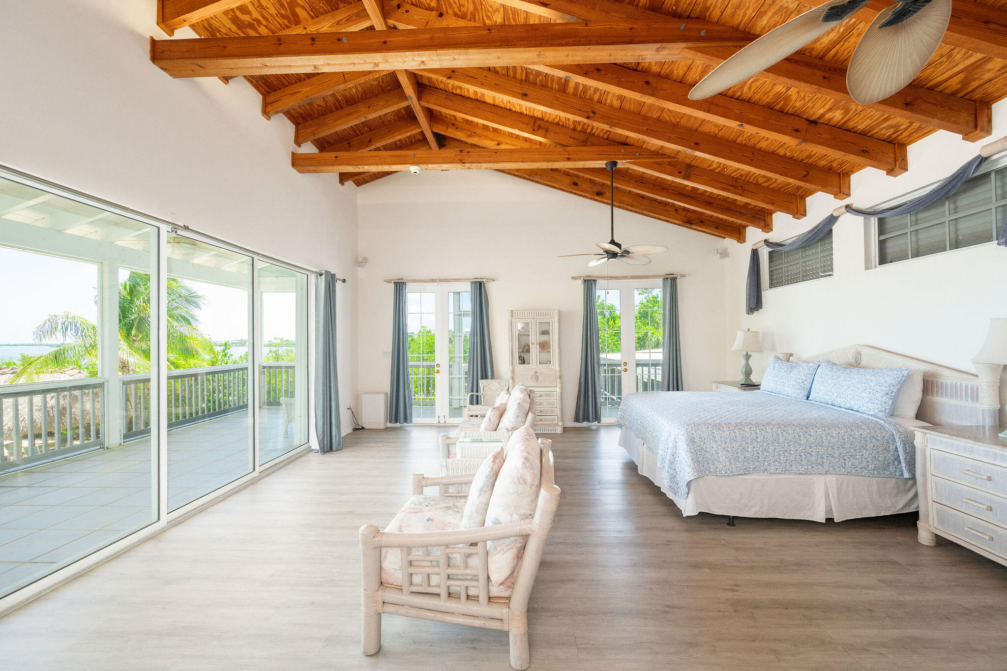 Furnished bedroom with exposed wood beams, a king bed, and sliding doors to a balcony overlooking water.