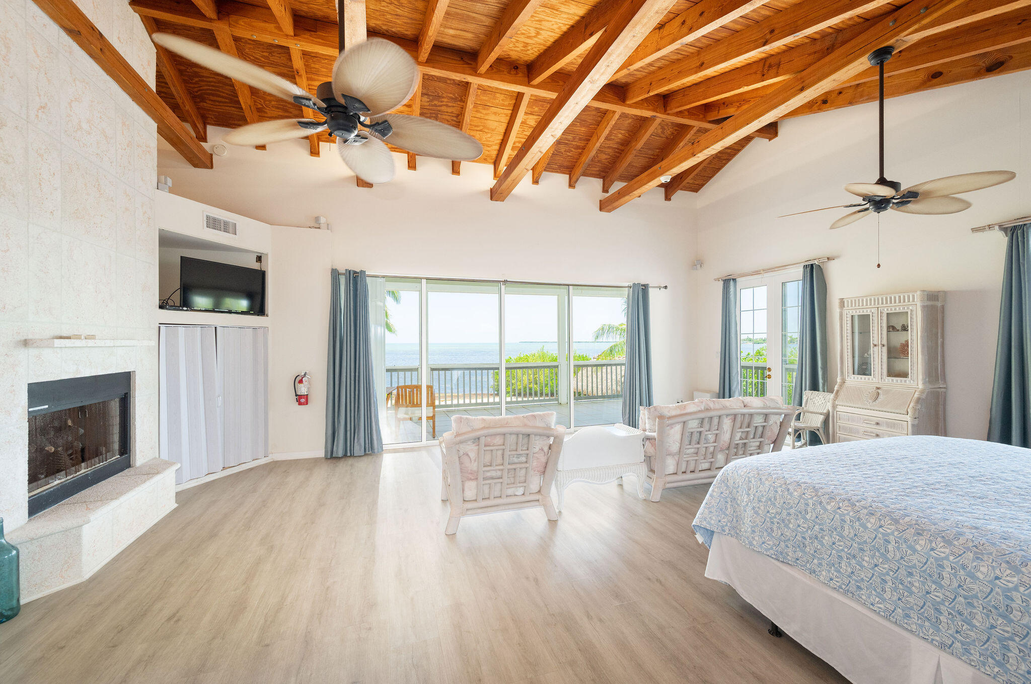 Bedroom with a fireplace, exposed wood beams, and ocean views through sliding glass doors.