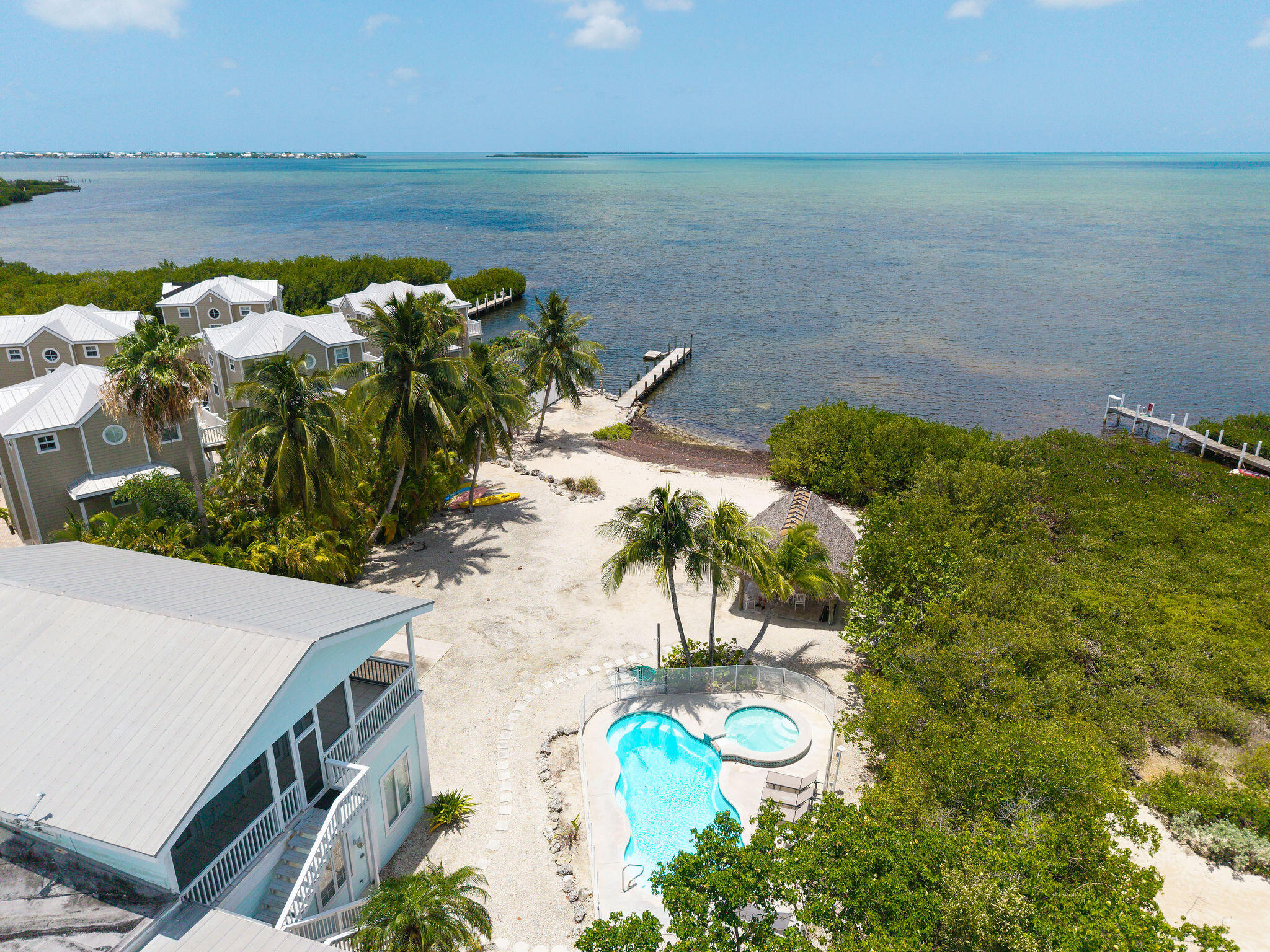 Aerial view of a waterfront home with a pool, sandy grounds, palm trees, and private docks.