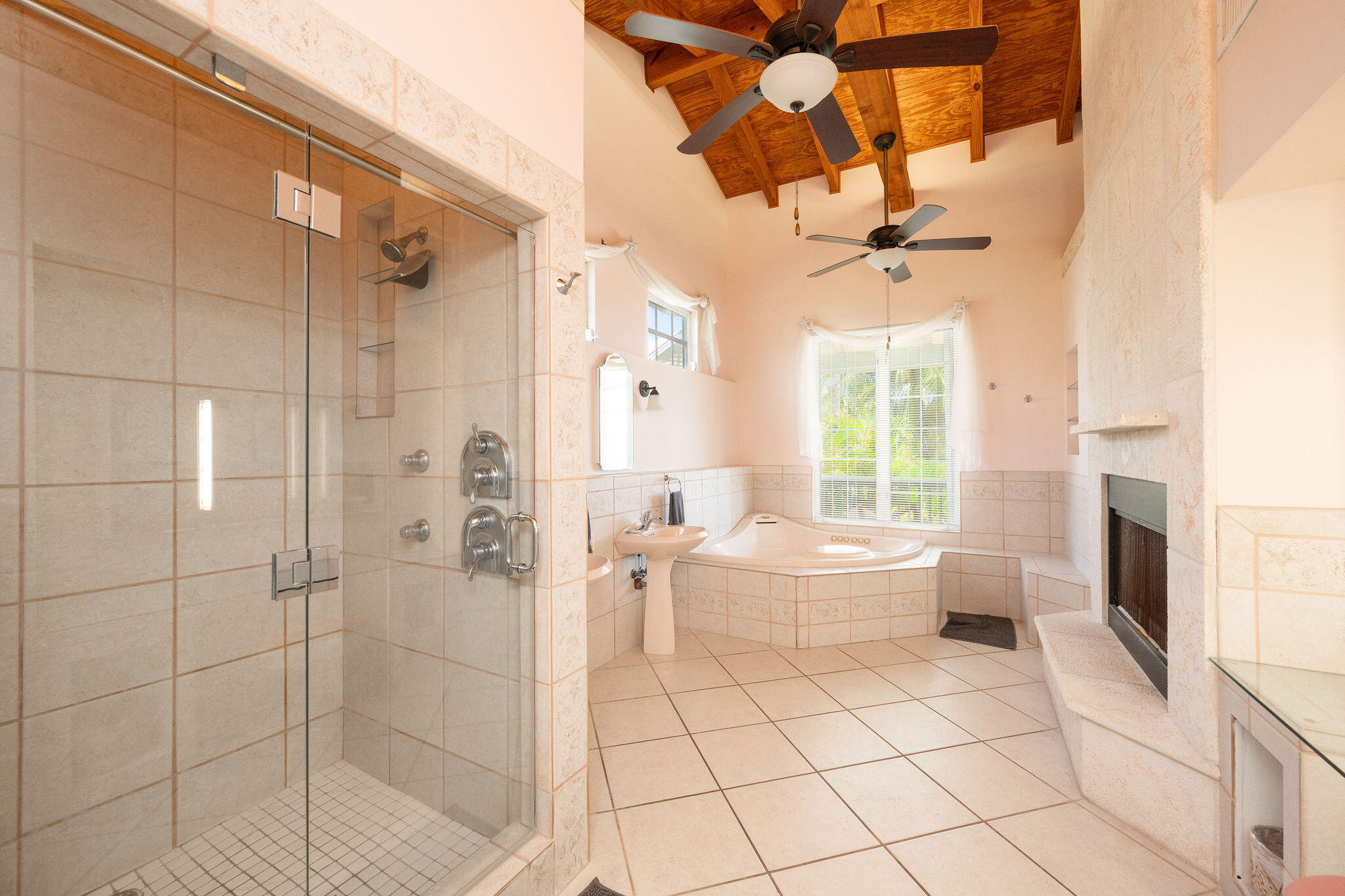 Bathroom with glass shower, corner soaking tub, exposed wood ceiling, and built-in fireplace.
