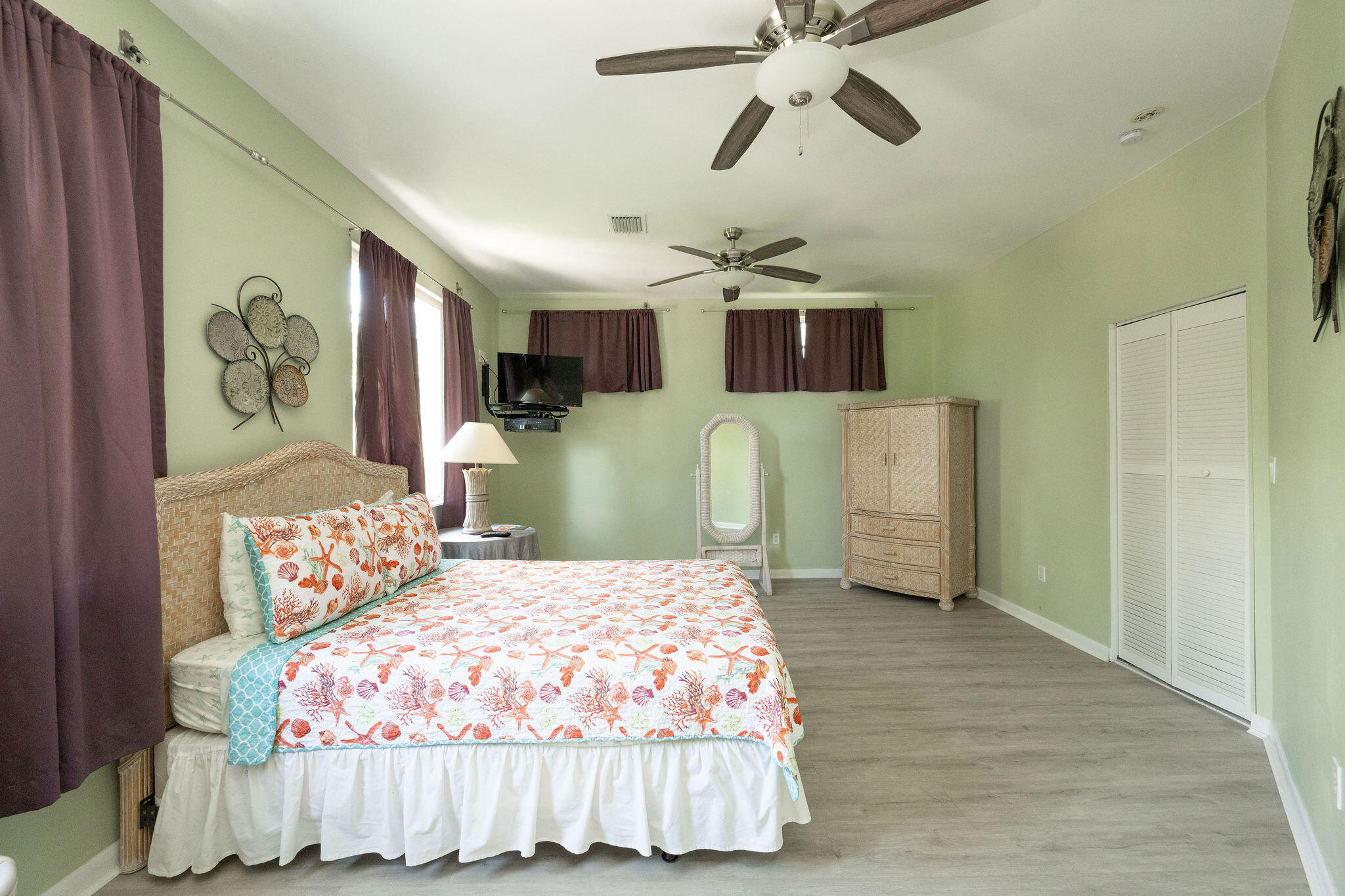 Furnished bedroom with a coral-patterned quilt, purple curtains, and pale green walls.