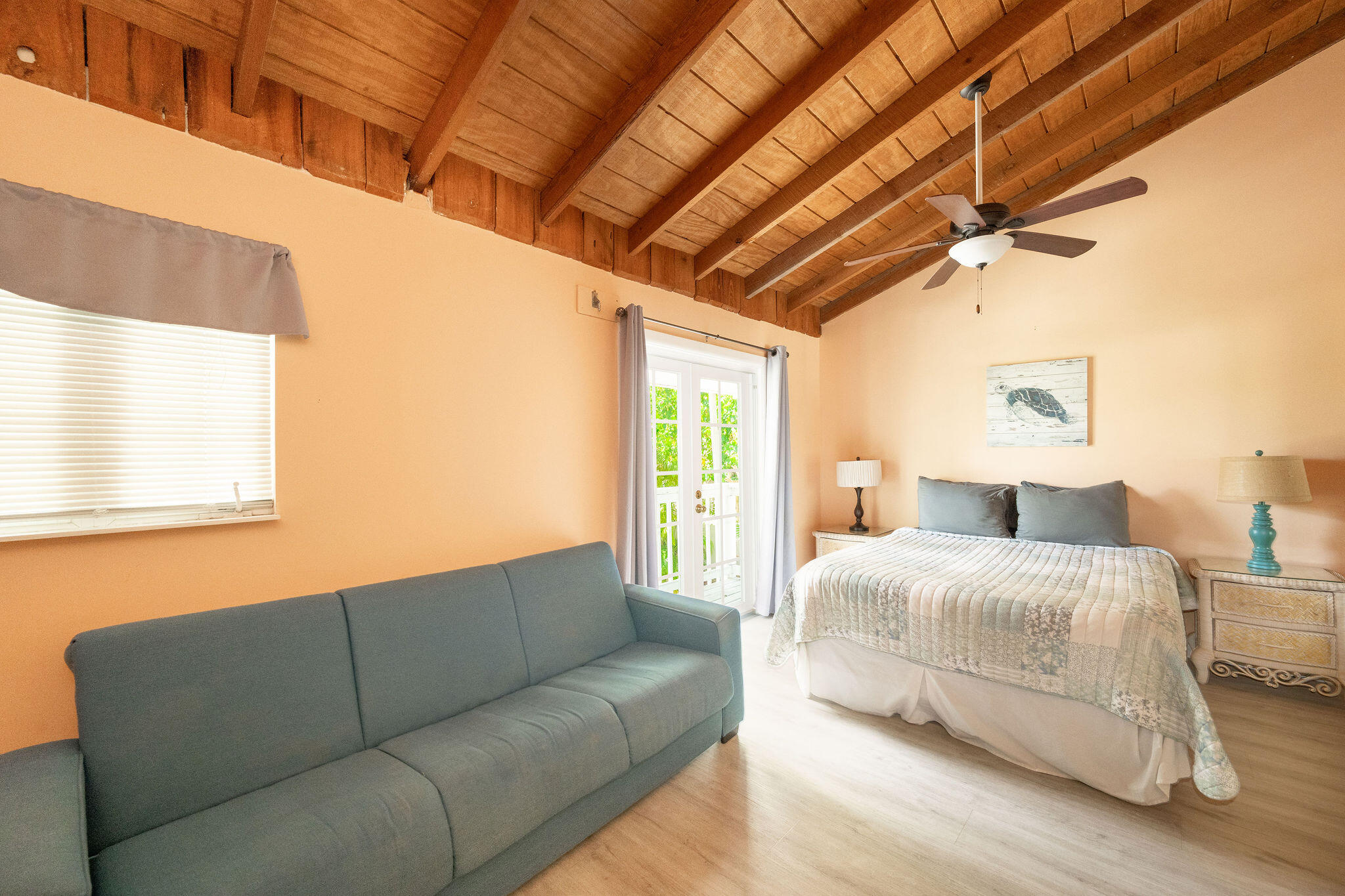 Bedroom with a gray sofa, French doors, and a vaulted exposed-wood ceiling.
