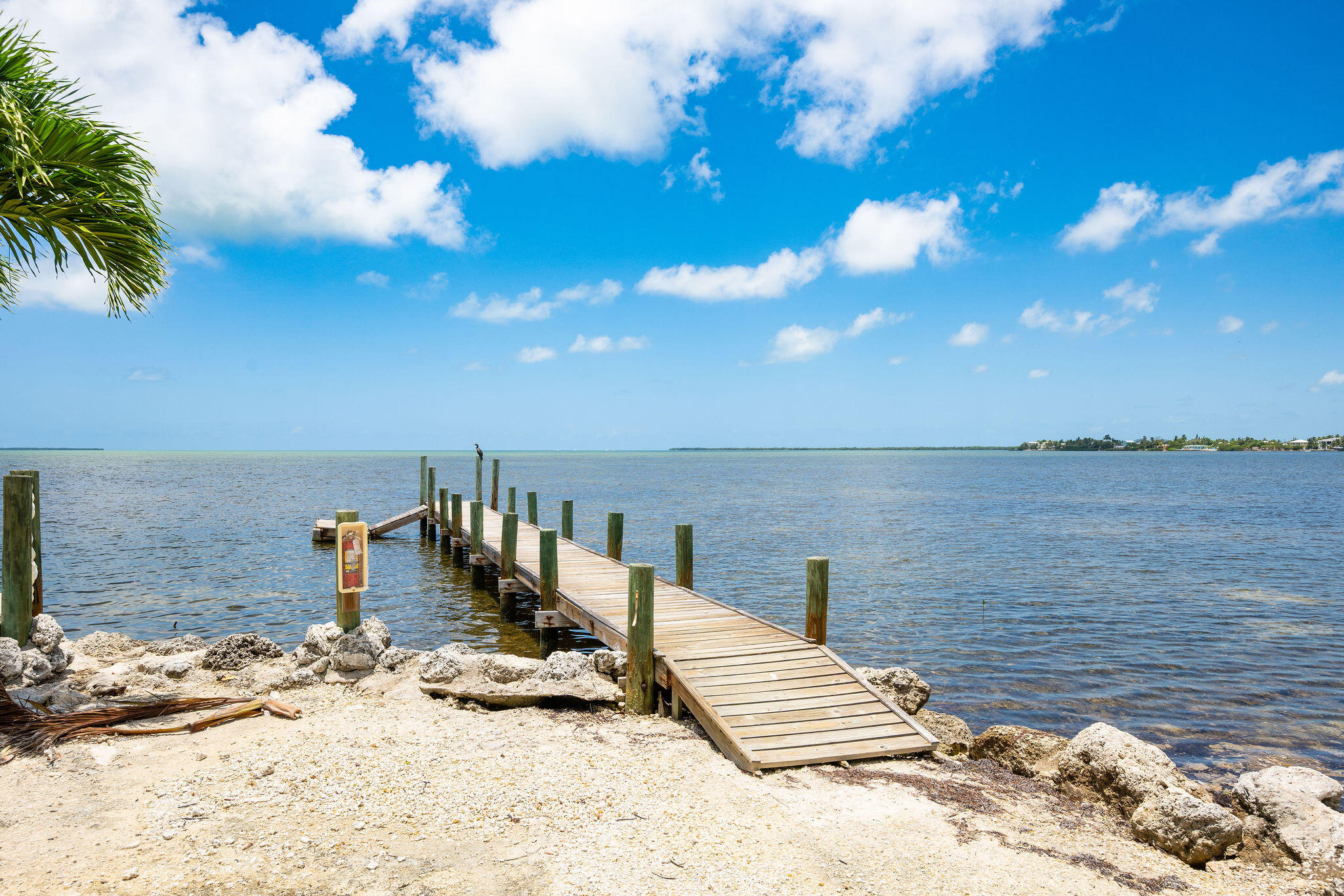 A wooden dock extends from a rocky shoreline into calm coastal water.