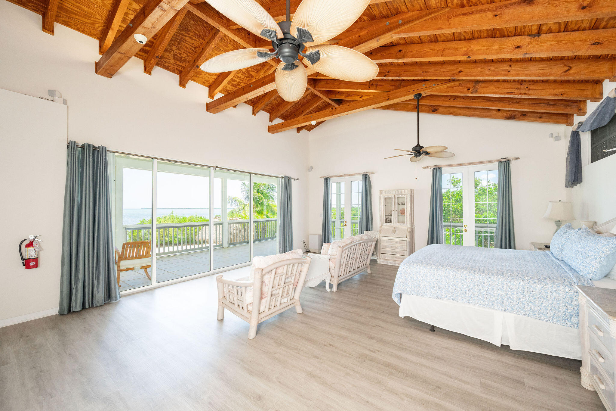 Bedroom with exposed wood beams, a sitting area, and sliding doors to a balcony overlooking the water.