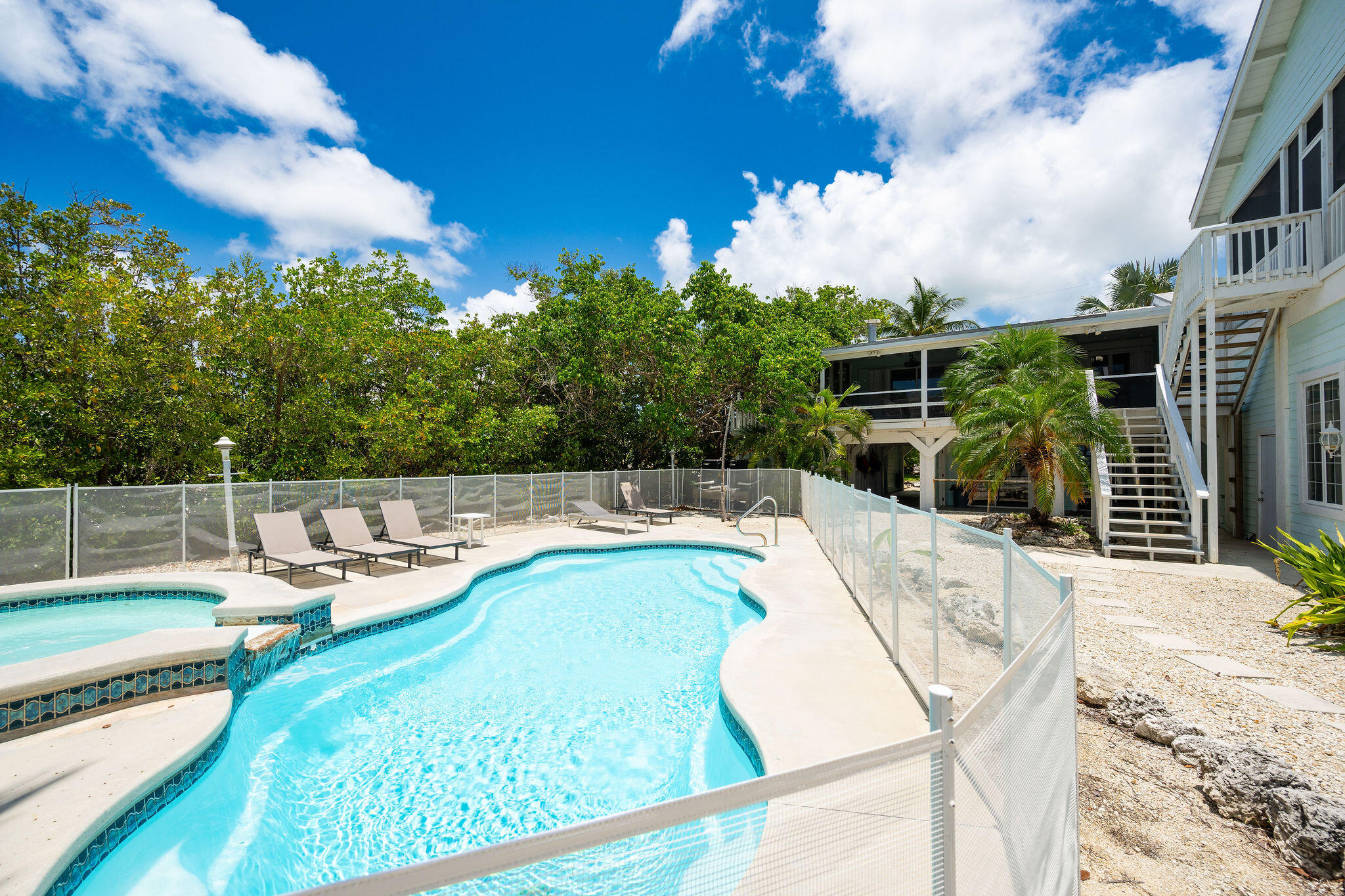 Curved swimming pool and raised spa beside an elevated home, with lounge chairs and tropical greenery.