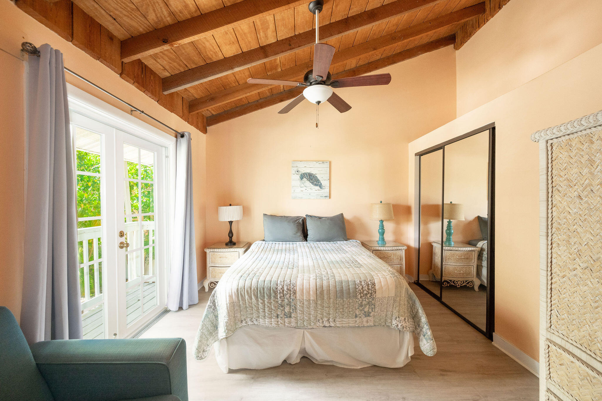 Furnished bedroom with exposed wood ceiling beams and glass doors opening onto greenery.