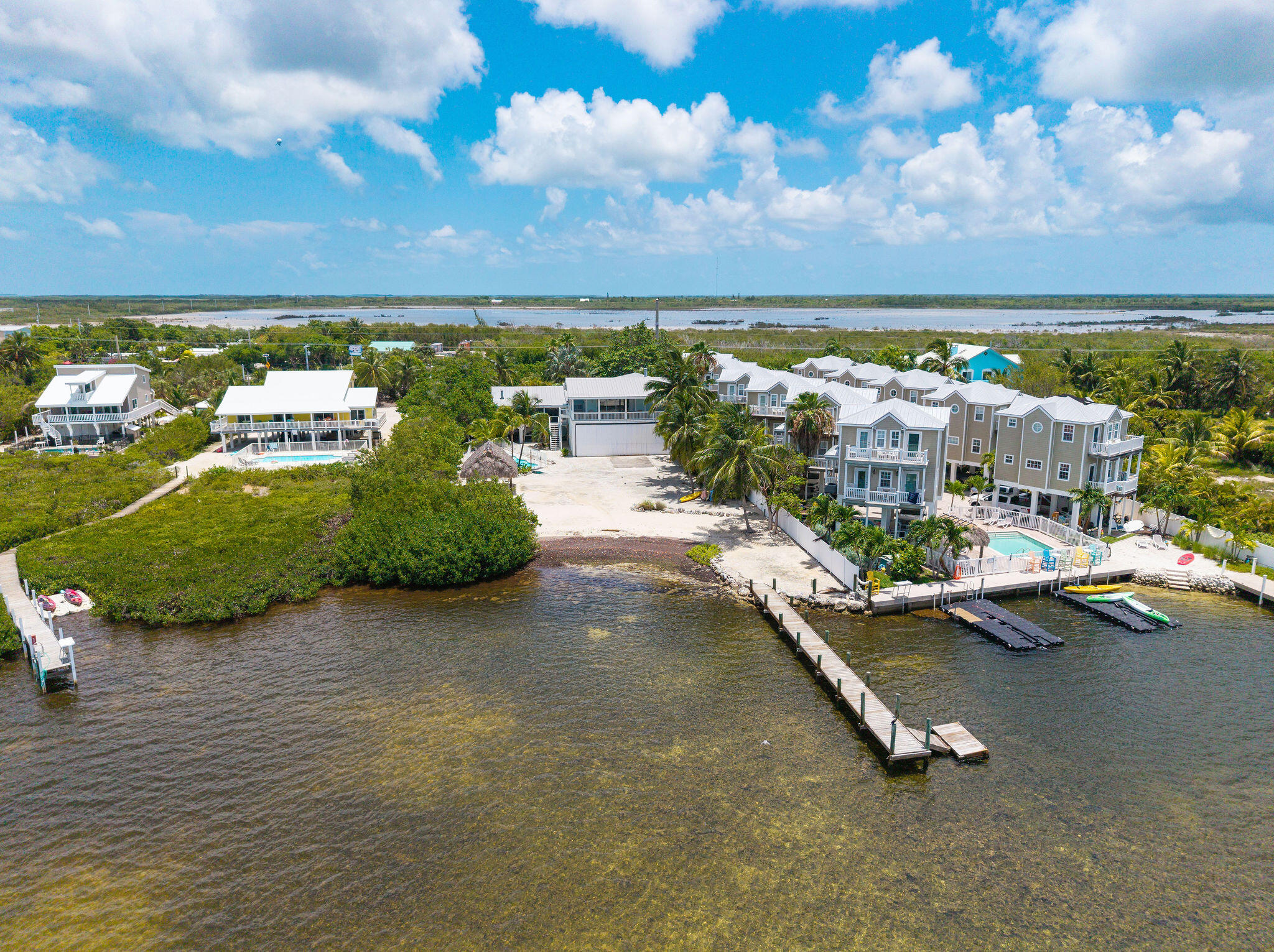 Waterfront homes and pool beside a shallow channel, with a long dock extending into the water.