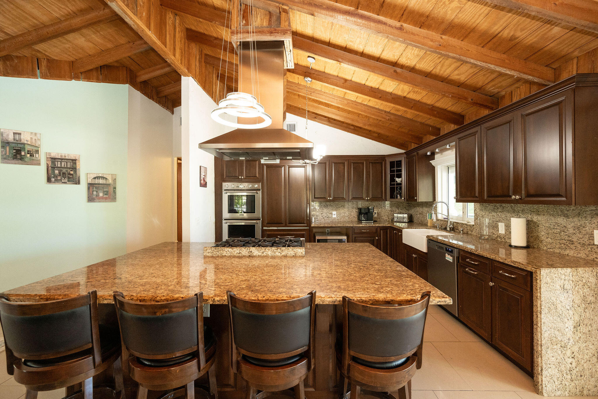Kitchen with a granite island, four bar stools, dark wood cabinets, and a vaulted wood-beam ceiling.