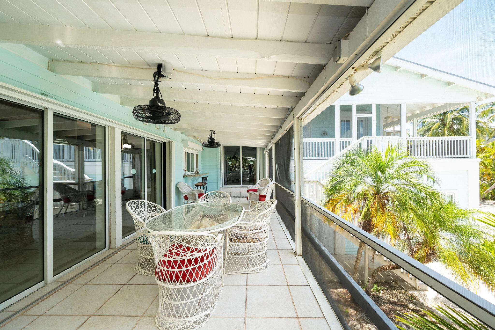 Screened porch with white wicker dining set, ceiling fans, and palm trees beyond the railing.