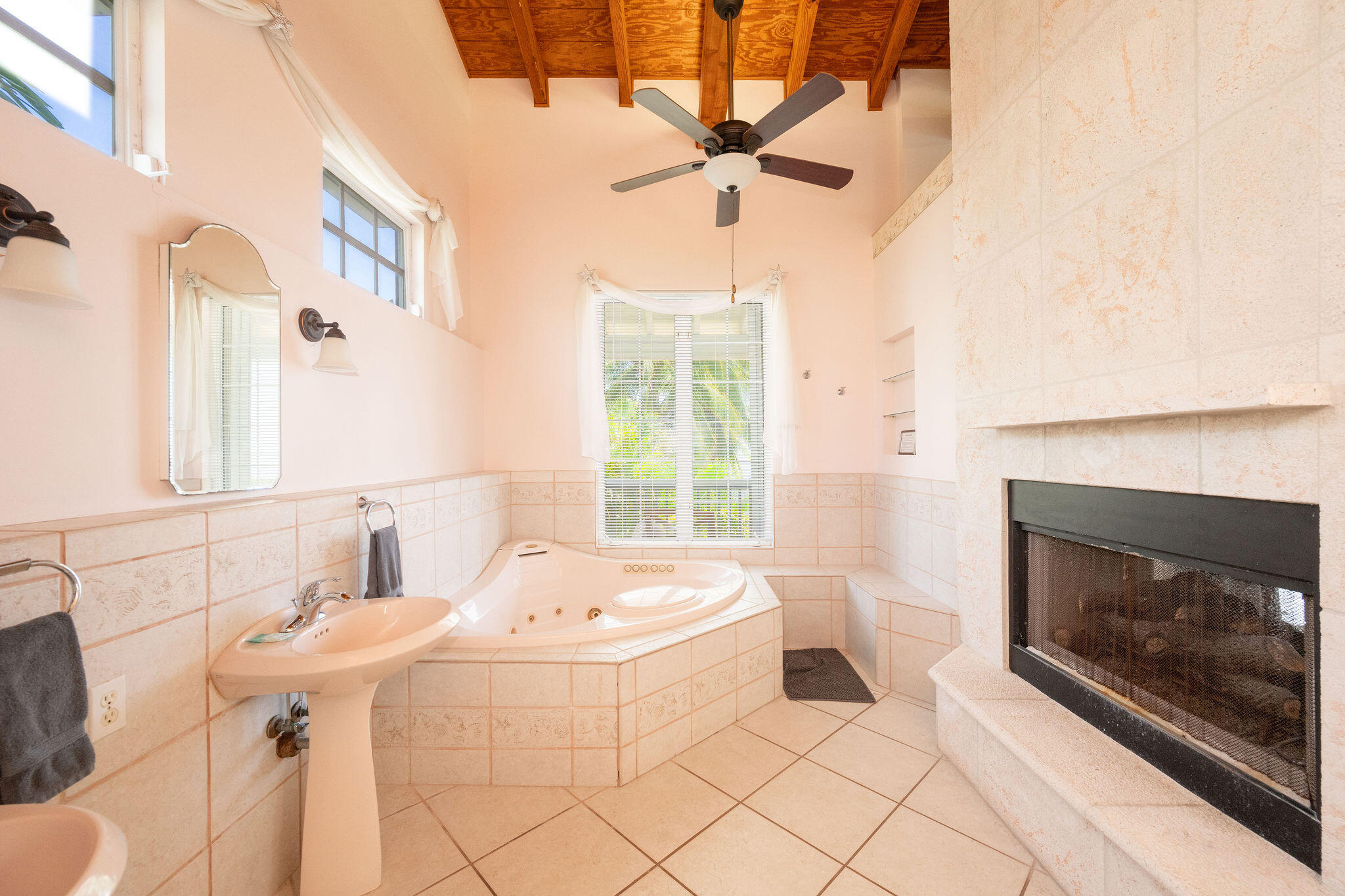 Bathroom with a corner whirlpool tub, pedestal sink, and large stone fireplace.