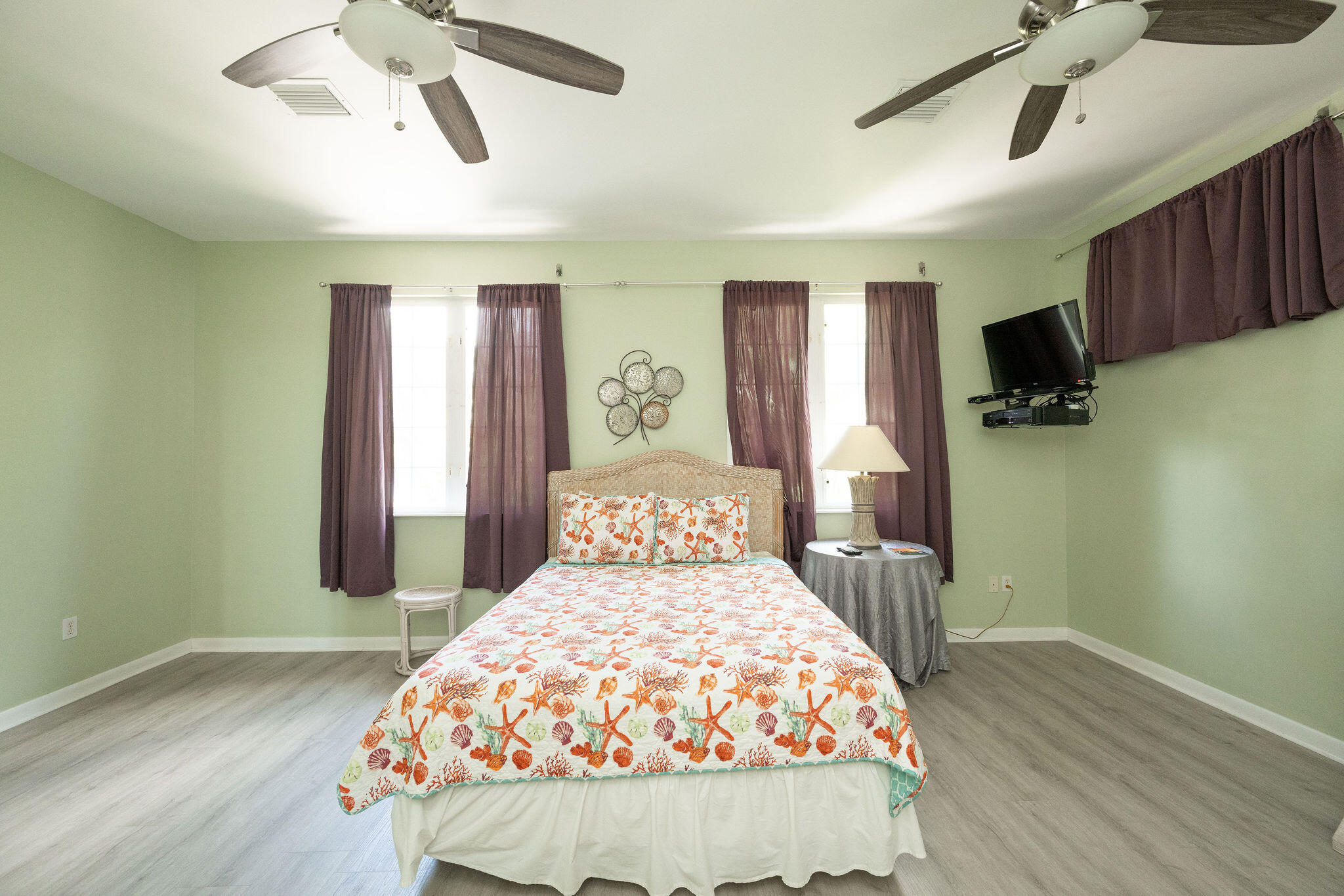 Bedroom with seashell-print bedding, purple curtains, and two ceiling fans.