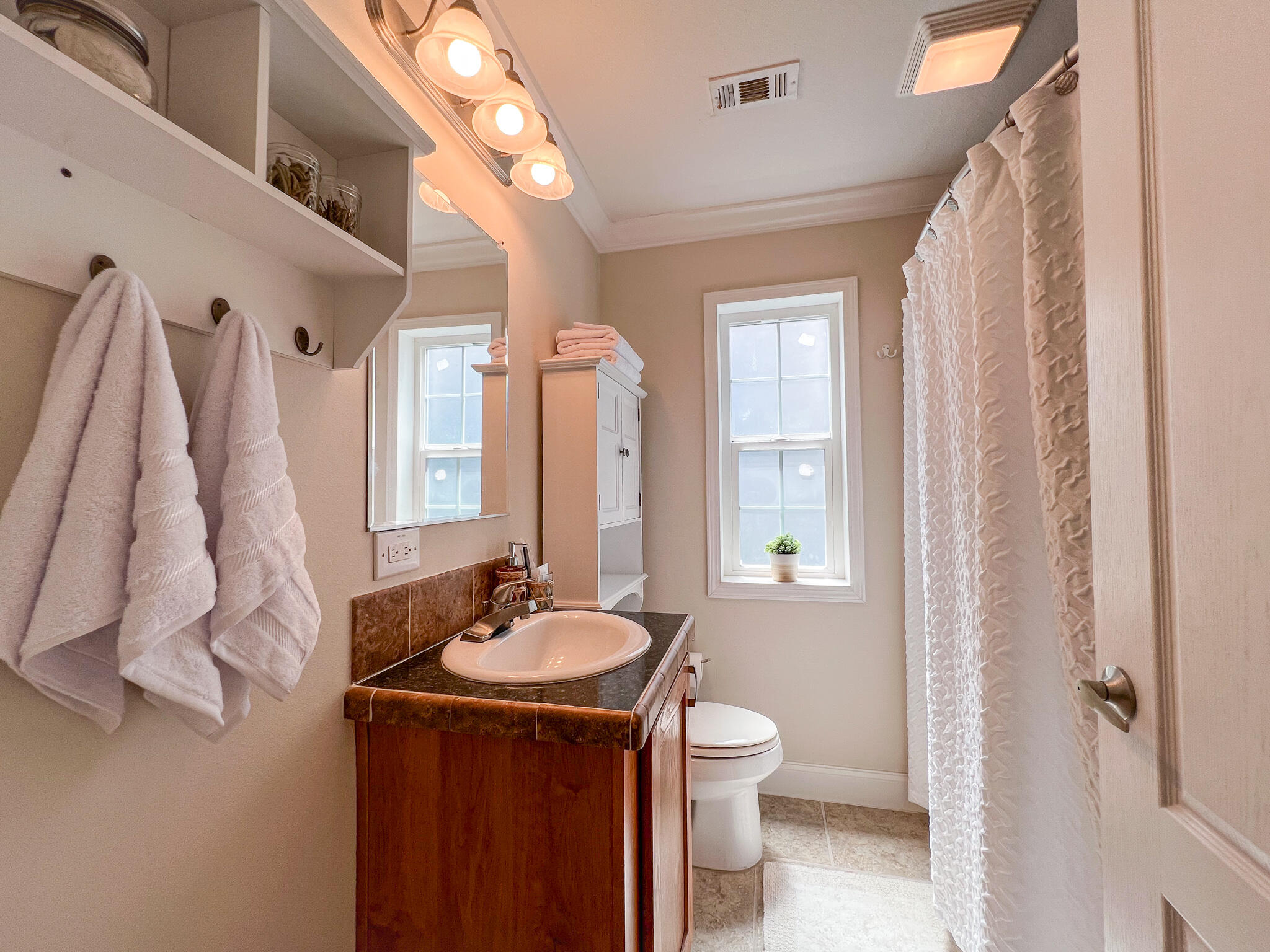 Bathroom with a wood vanity, oval sink, white shower curtain, and two windows.