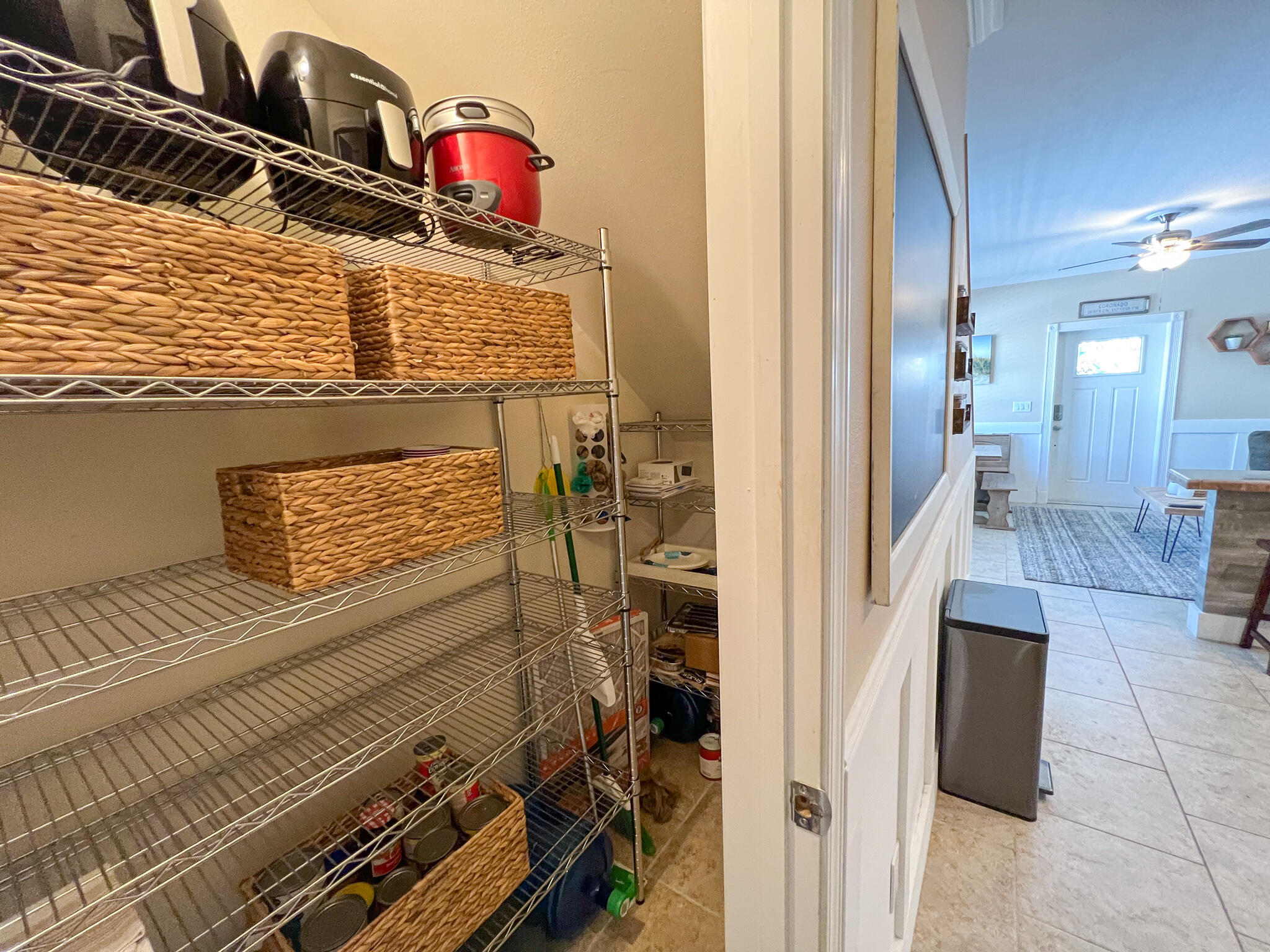 Walk-in pantry with wire shelving and woven baskets beside a bright tiled entryway.