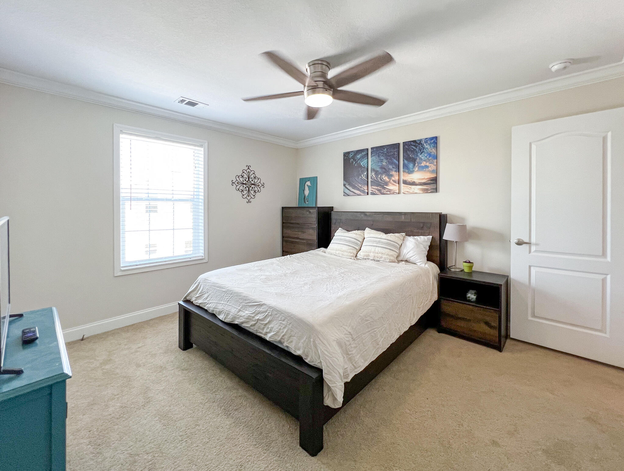 Furnished bedroom with a dark wood bed, white bedding, window blinds, and coastal artwork.