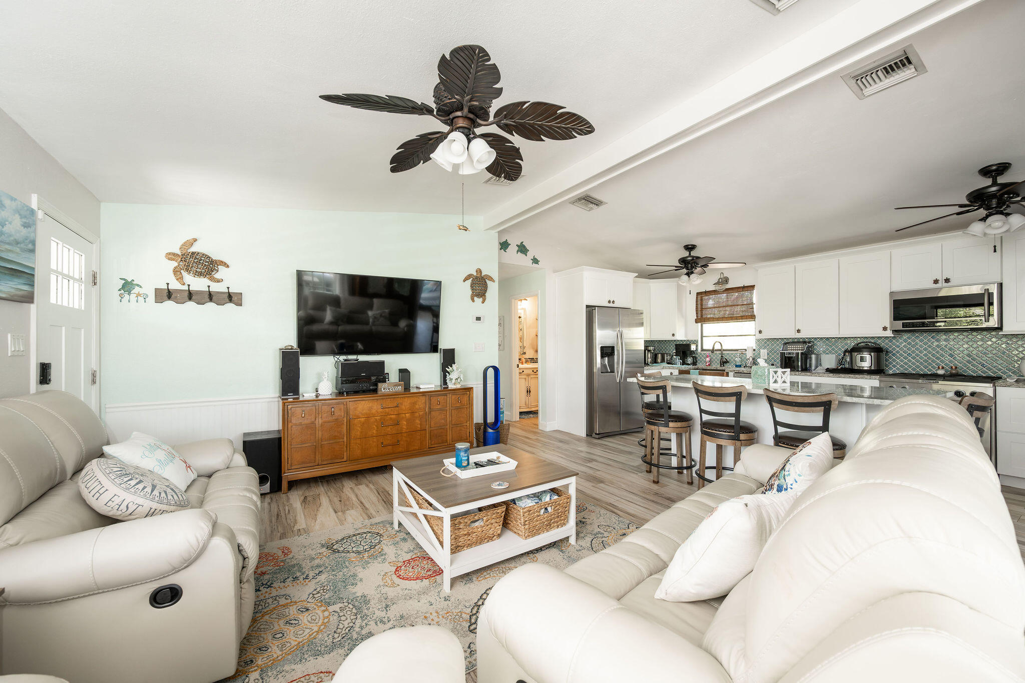 Open-plan living room and kitchen with white leather sofas and a blue patterned backsplash.