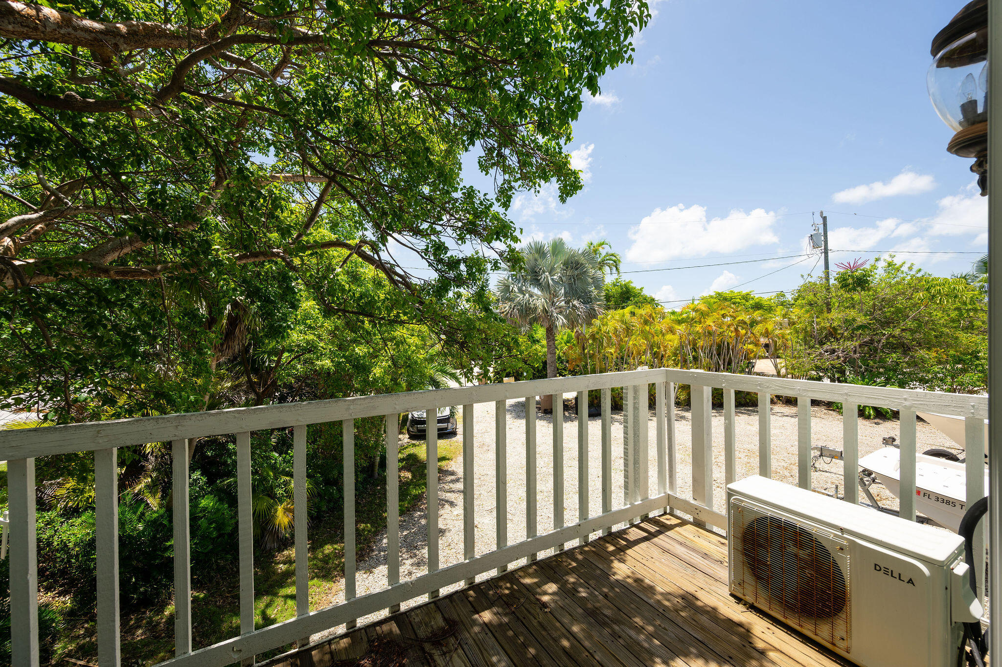 Wooden deck overlooking a palm-lined gravel parking area, with an outdoor air-conditioning unit beside the railing.