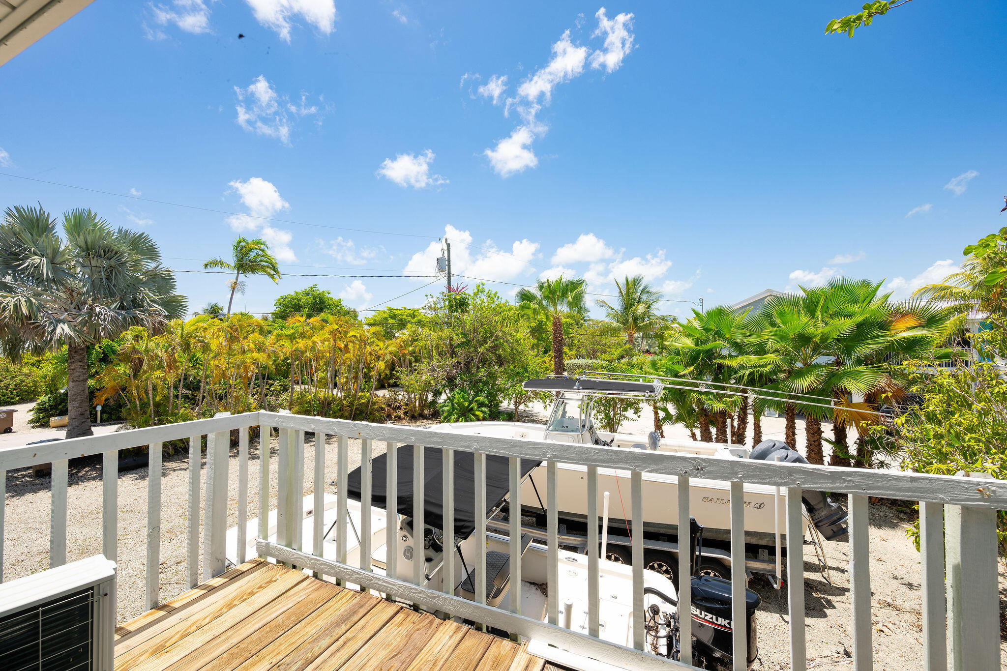 Deck view over a boat on a trailer, with tropical palms and a gravel lot.