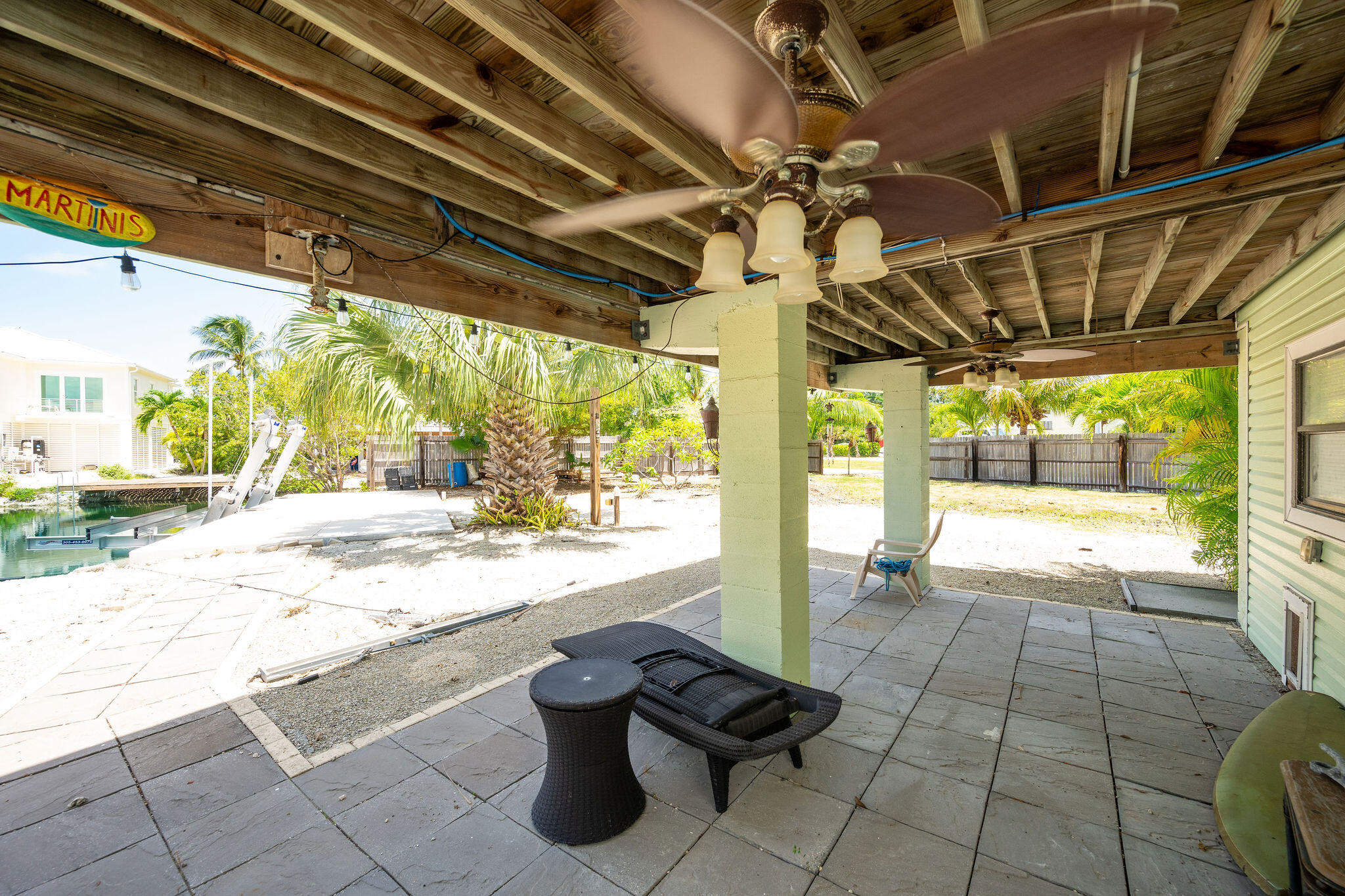 Covered patio with ceiling fans and wicker seating overlooking a palm-lined canal and boat lifts.