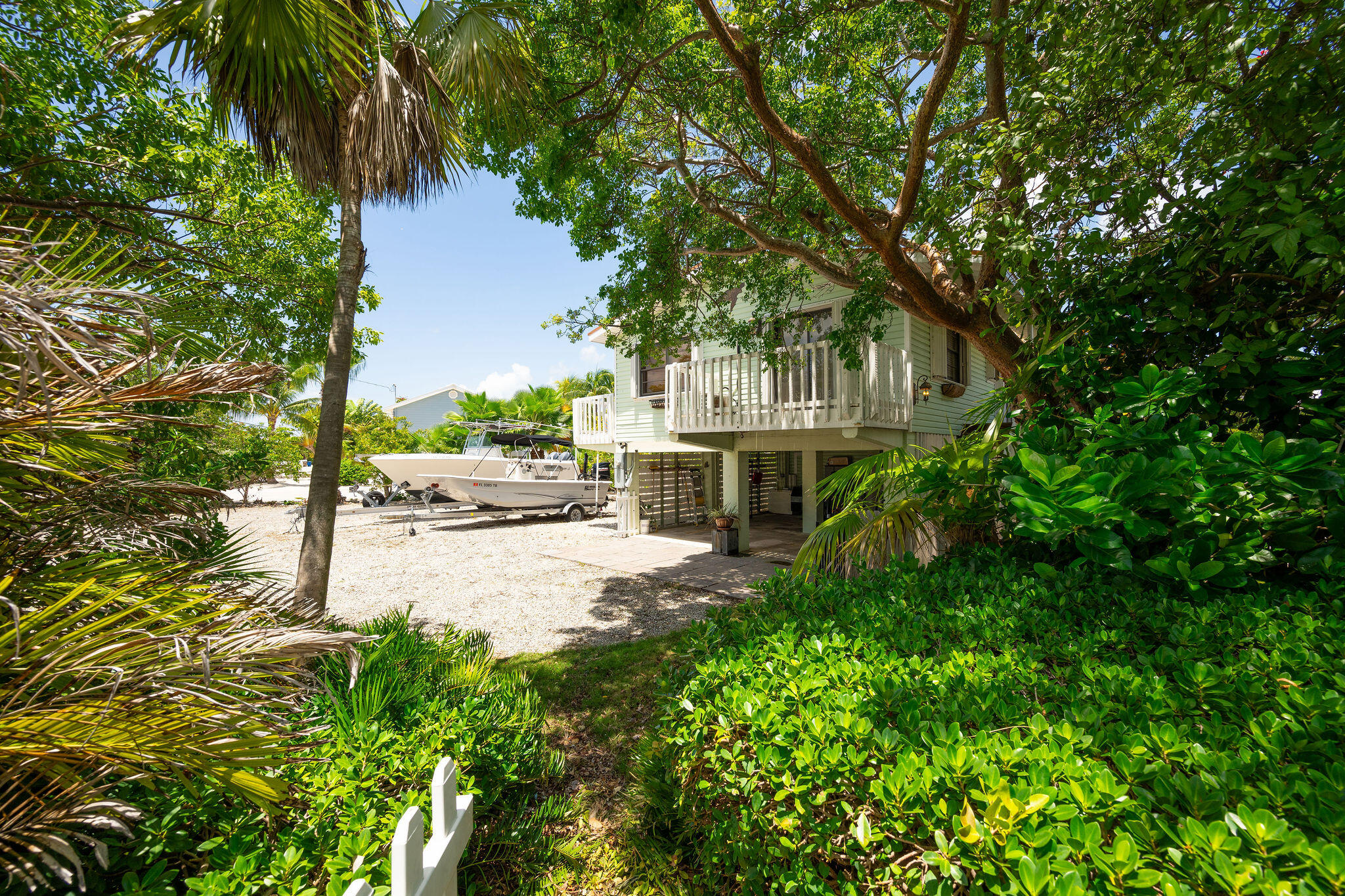 Elevated coastal home with a boat parked beside it amid dense tropical landscaping.