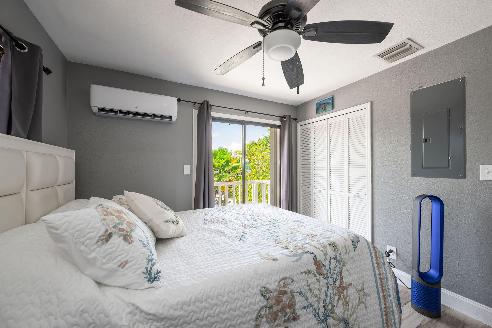 Bedroom with sea-life print bedding and sliding doors opening to a tropical balcony.