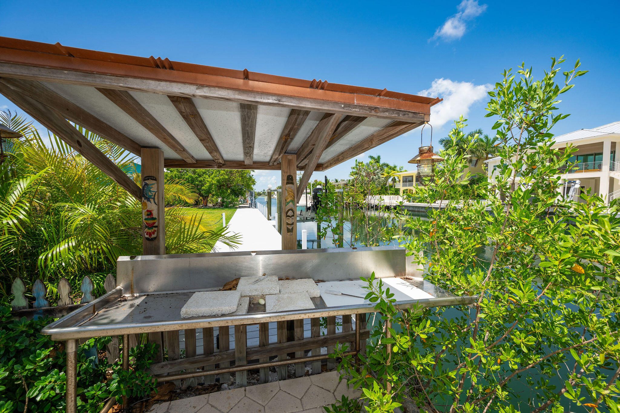 Covered canal-side dock with a stainless-steel fish-cleaning station and tropical greenery.