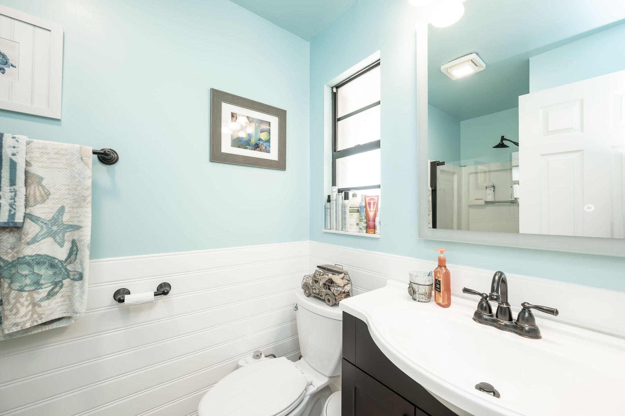 Bathroom with pale blue walls, white beadboard, dark vanity, and coastal-patterned towels.