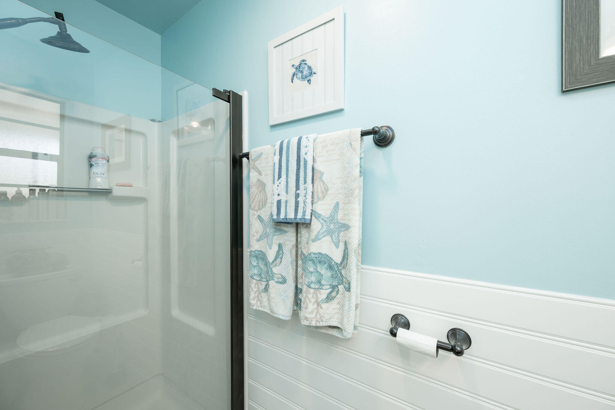 Bathroom shower with glass enclosure and blue sea turtle towels against aqua walls.