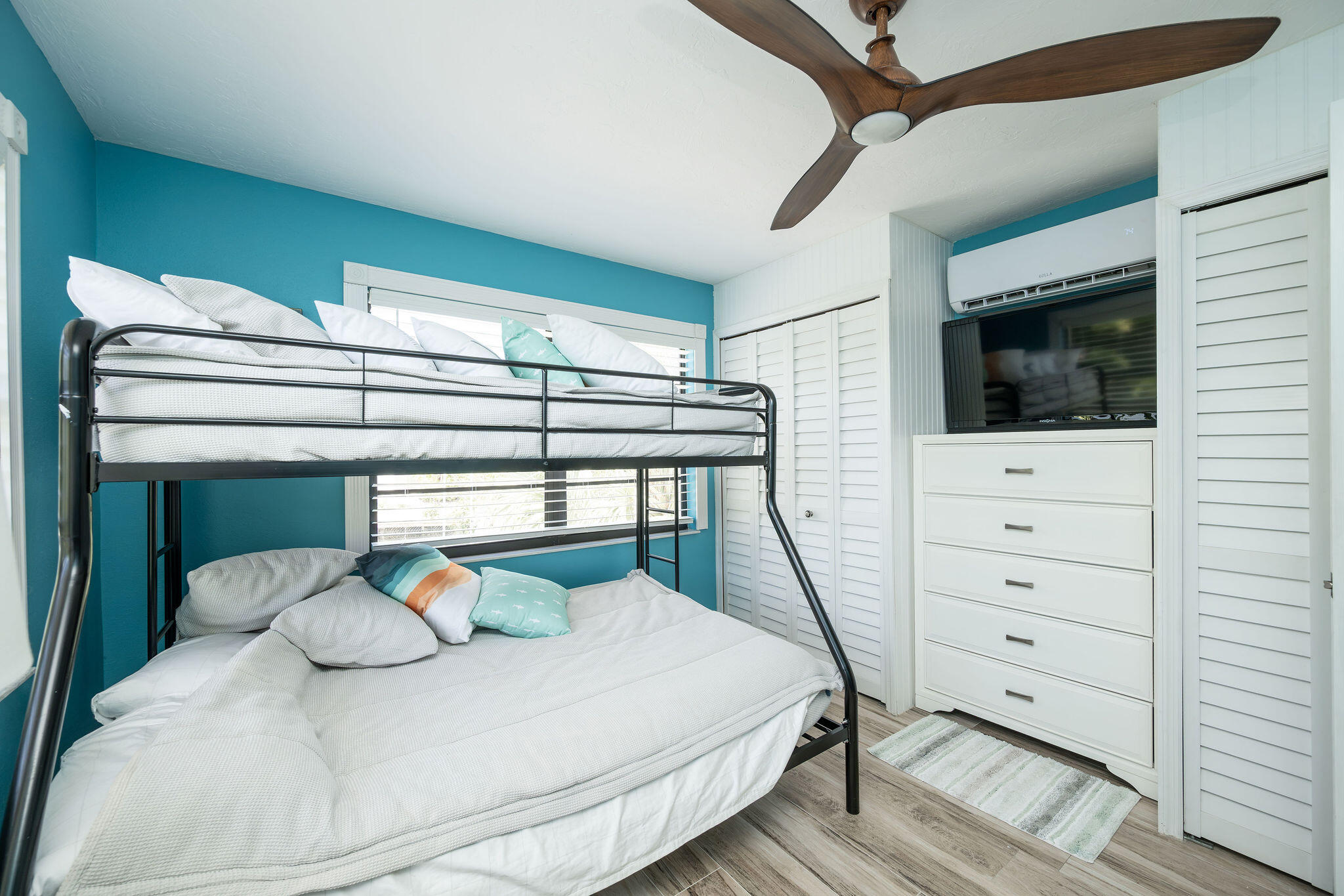 Bedroom with a black metal bunk bed, teal walls, and a TV above a white dresser.