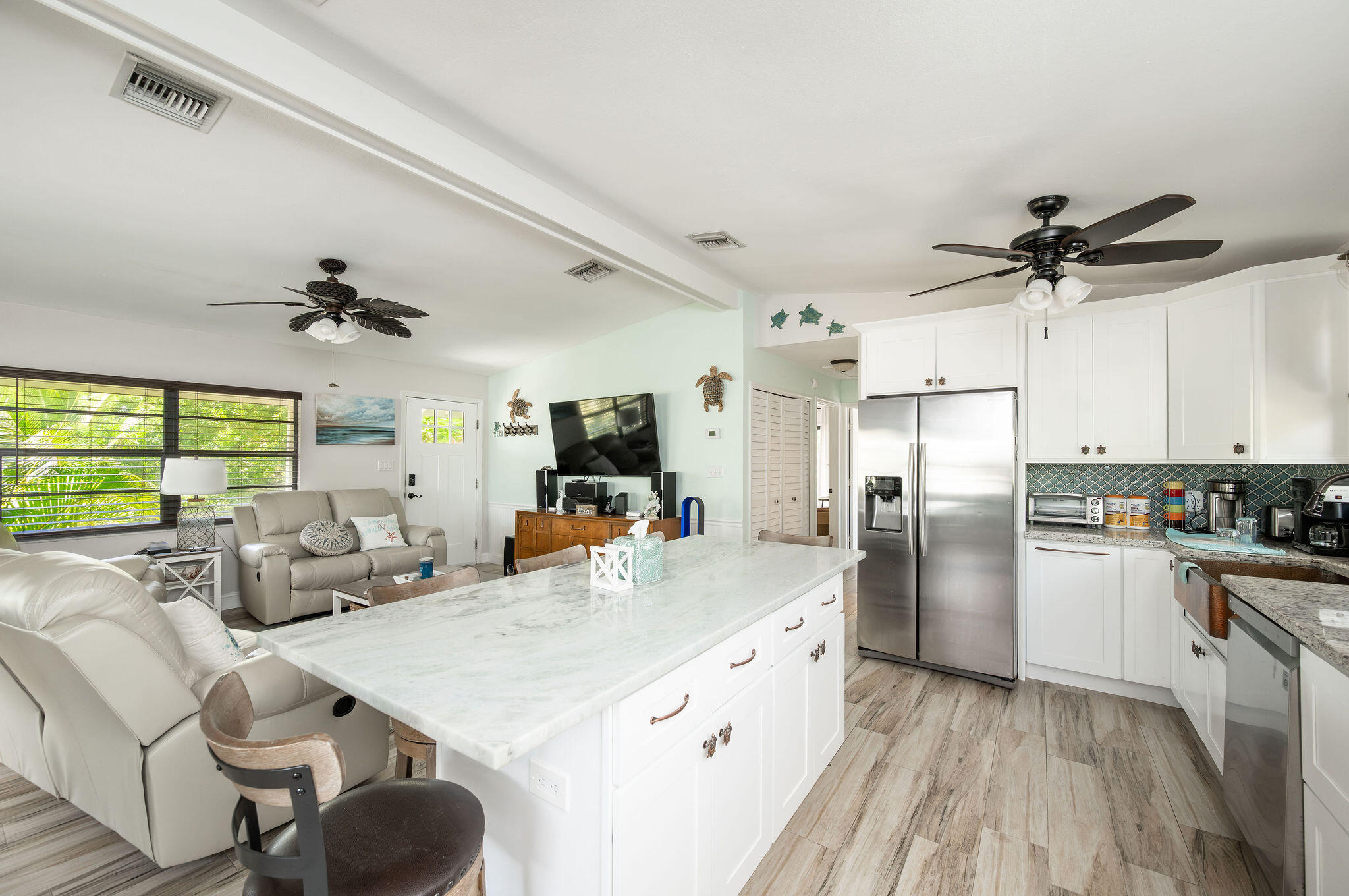 Open-plan kitchen and living room with a large marble island, white cabinetry, and stainless-steel refrigerator.