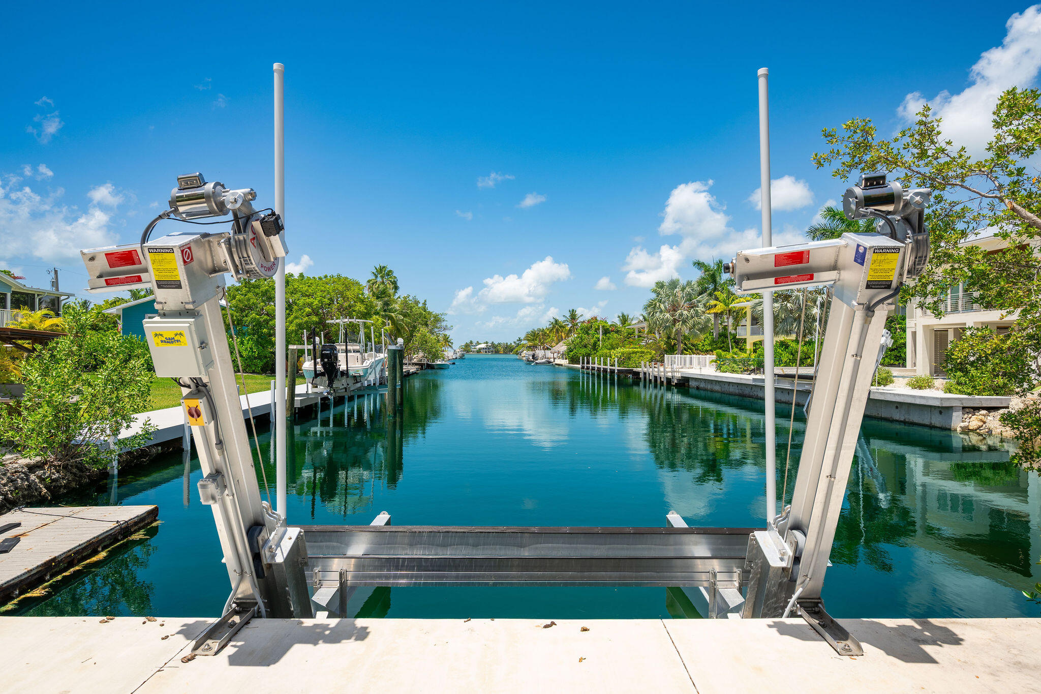 Waterfront canal framed by a metal boat lift, with docks and tropical homes along the banks.