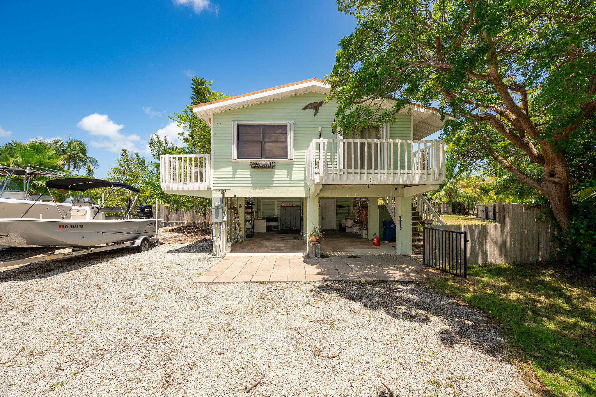 Pale green elevated home with white balconies, a boat on a trailer, and tropical trees.