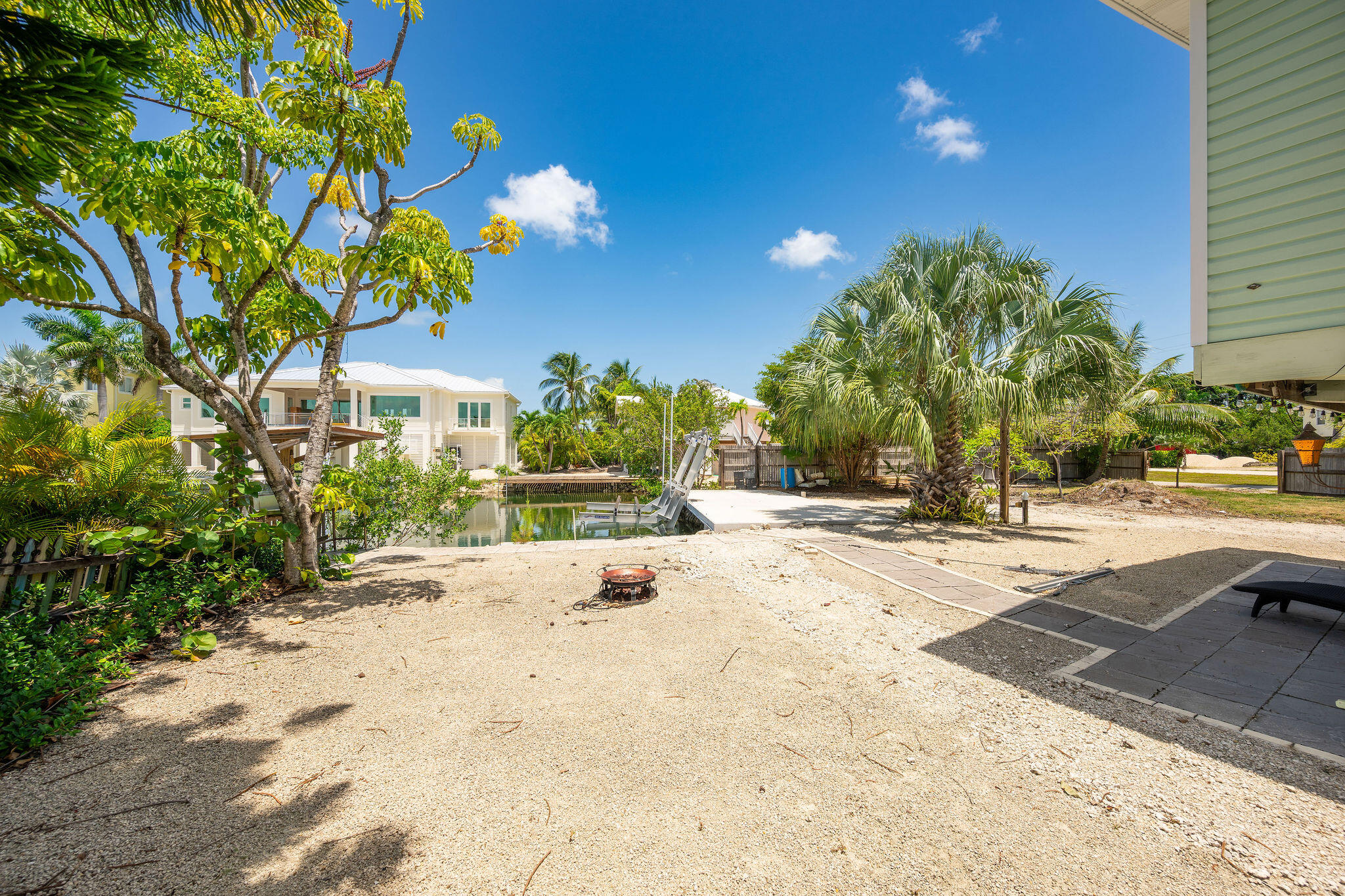 Sandy tropical backyard with a canal, boat lift, fire pit, and paved patio.