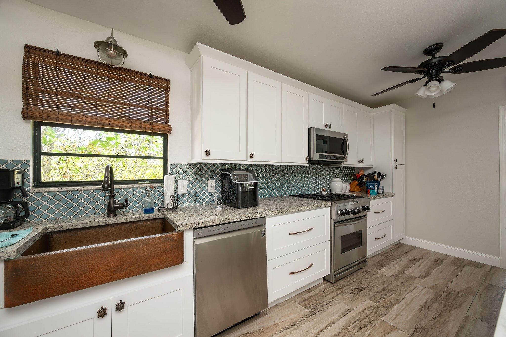 Kitchen with a copper farmhouse sink, patterned tile backsplash, white cabinets, and stainless steel appliances.