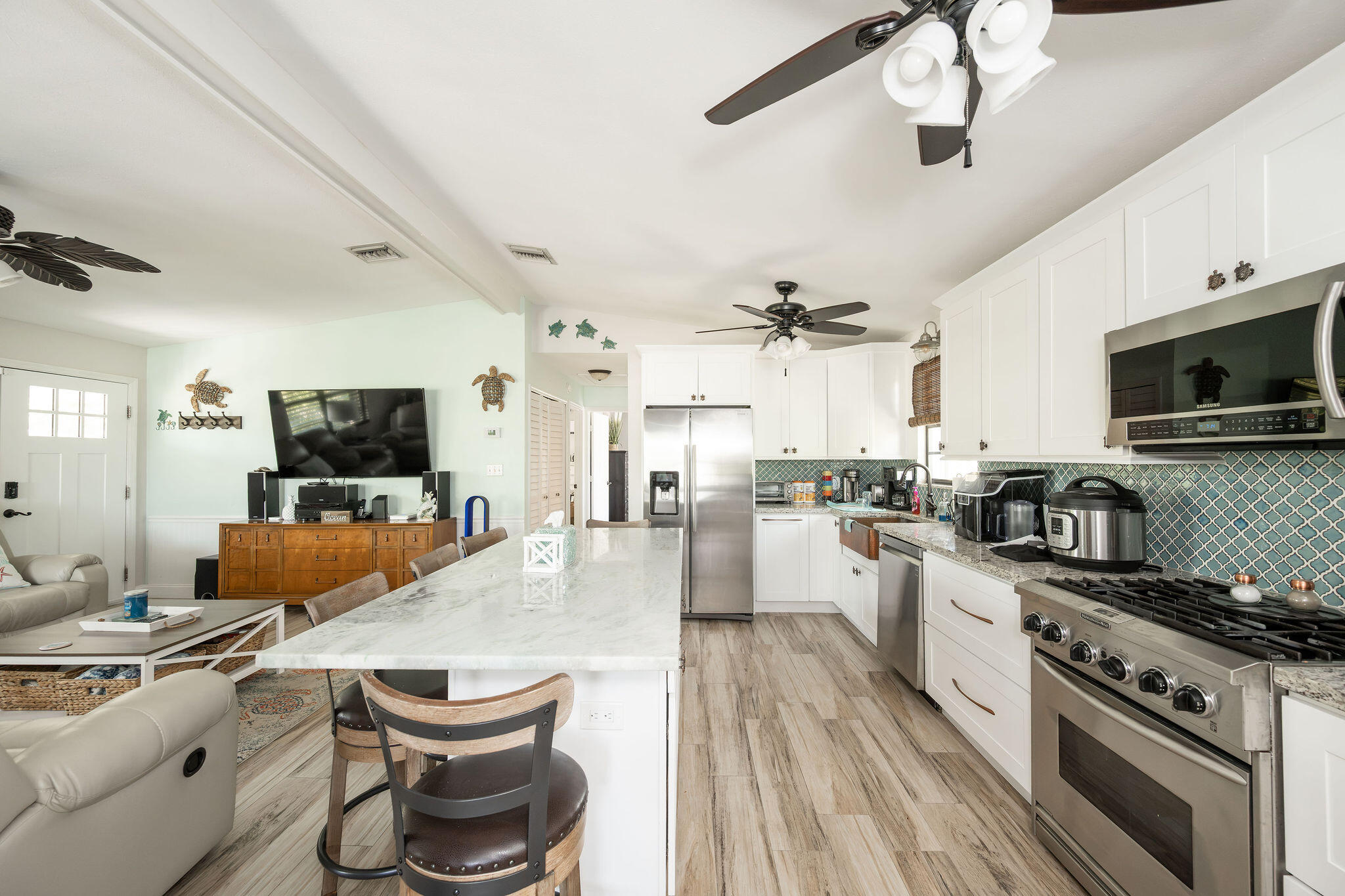Open-plan kitchen with a marble island, white cabinets, stainless appliances, and an adjoining living area.