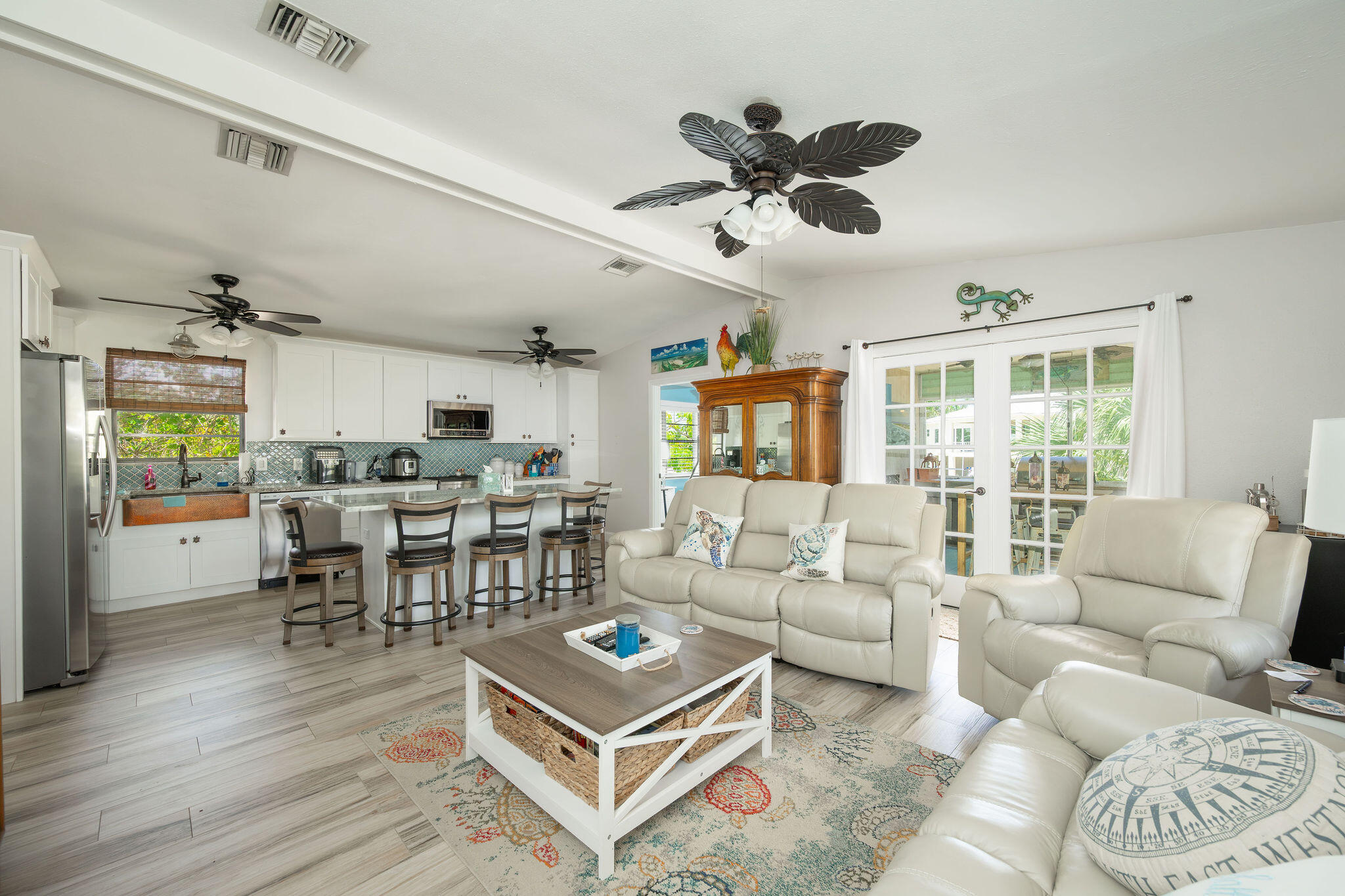Open-plan living room and kitchen with white leather seating, a bar island, and French doors.