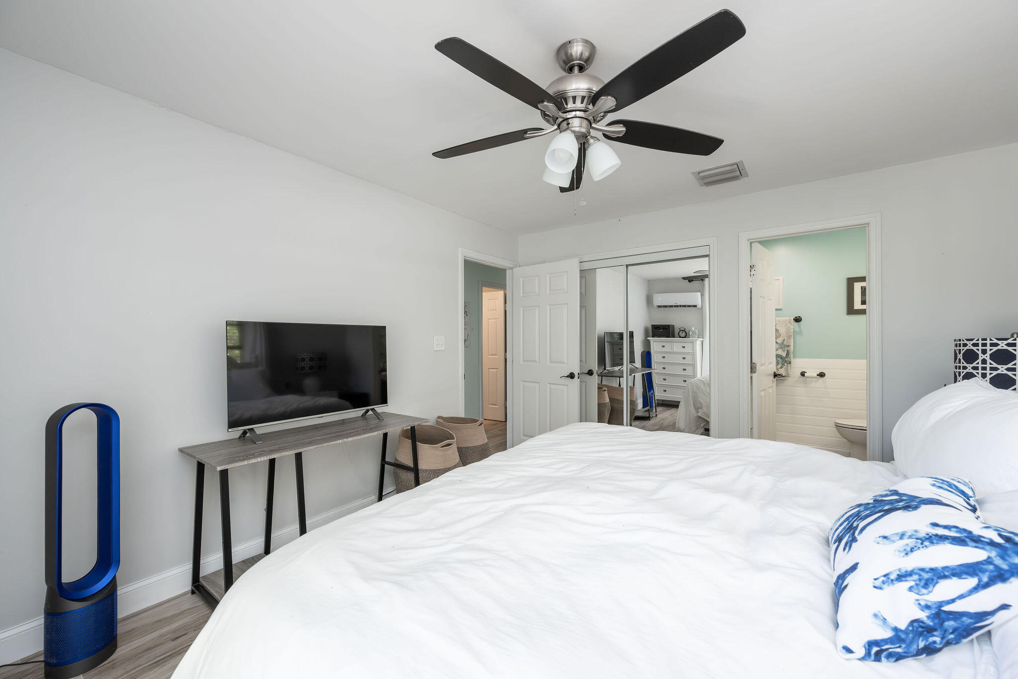 Bedroom with a white bed, ceiling fan, TV console, and open bathroom doorway.