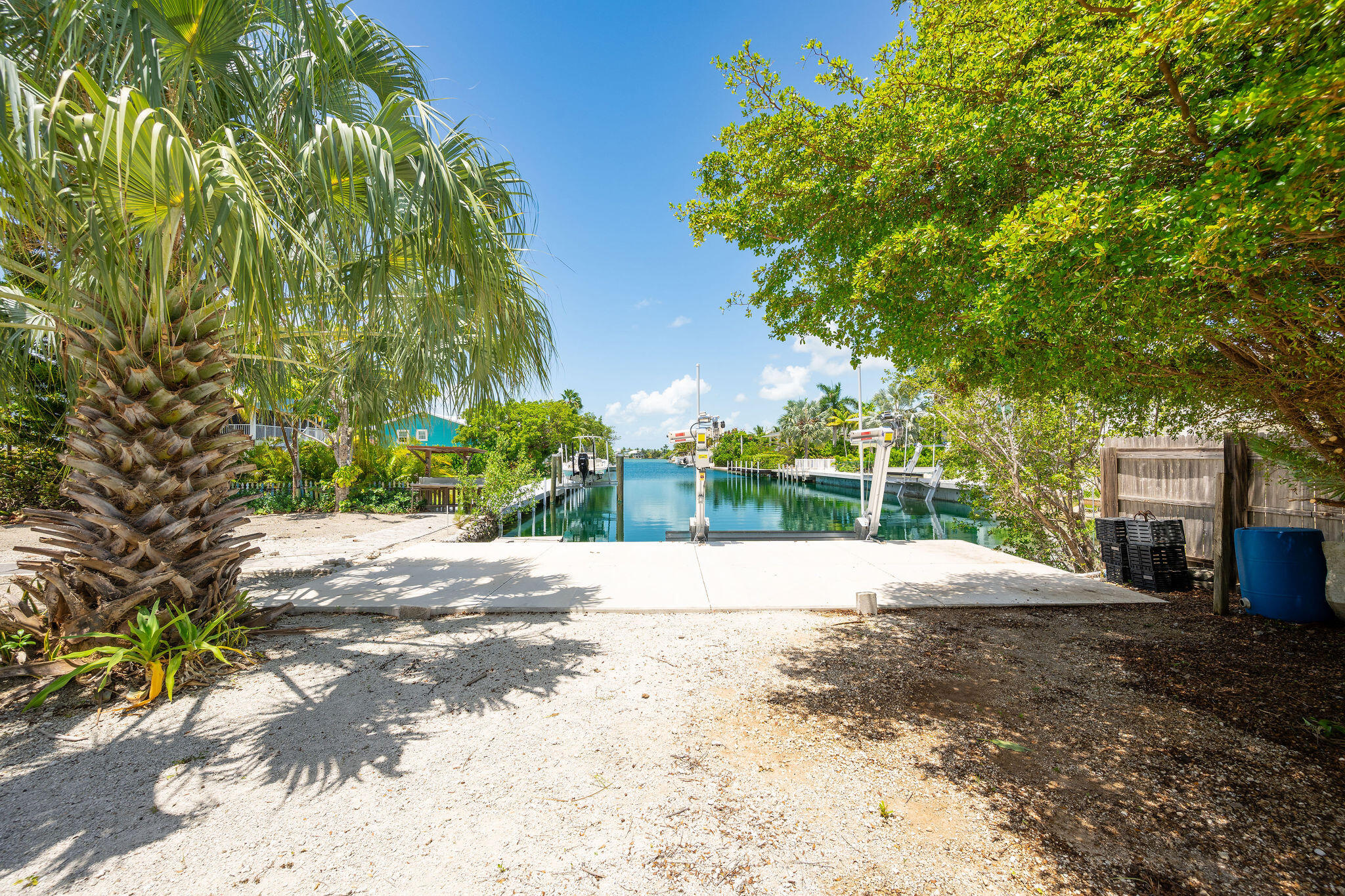 Canal waterfront with boat lifts, framed by palm trees and a shaded sandy yard.