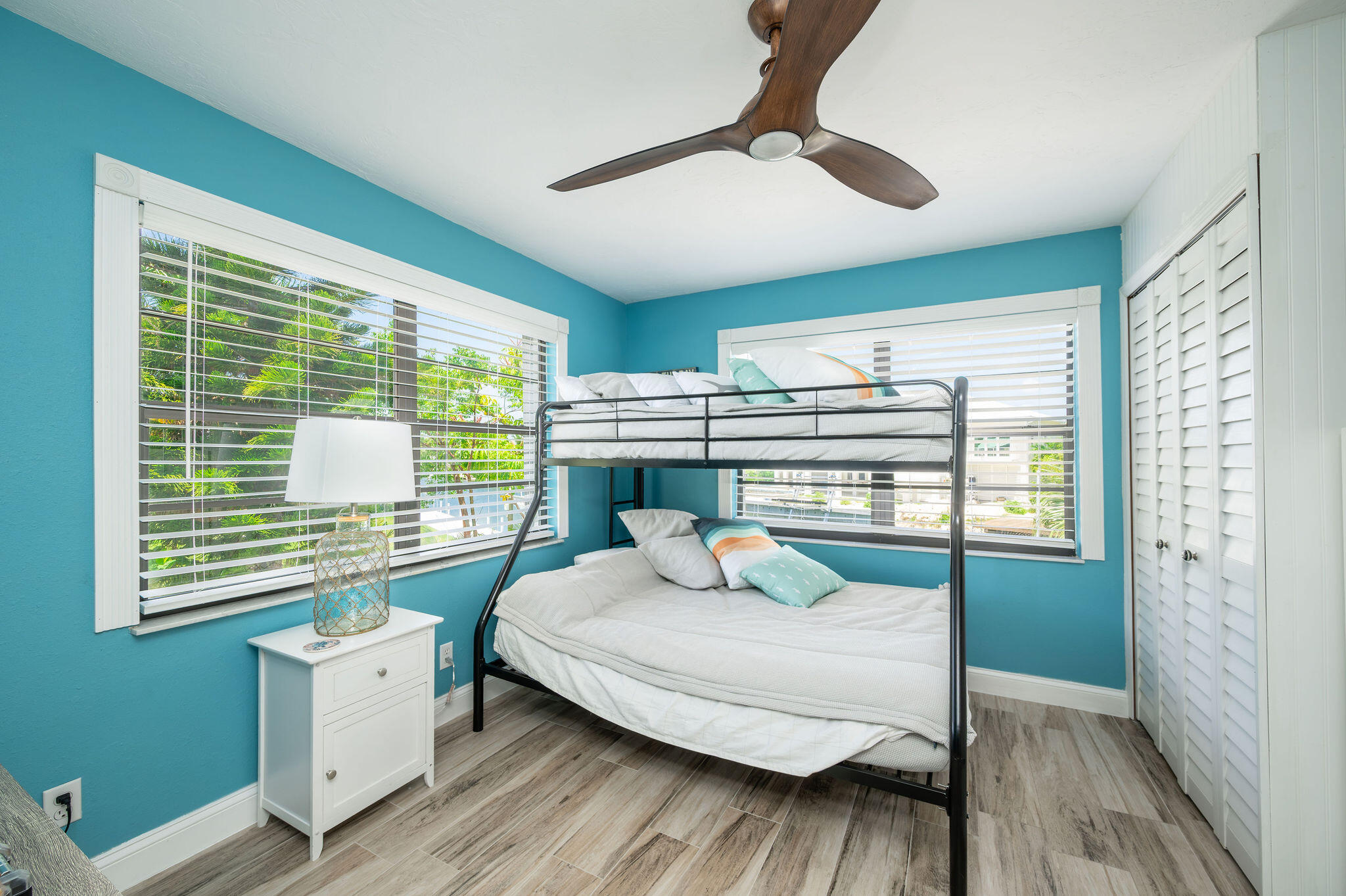 Bedroom with turquoise walls, a white-bedded bunk bed, plantation shutters, and gray wood-look flooring.