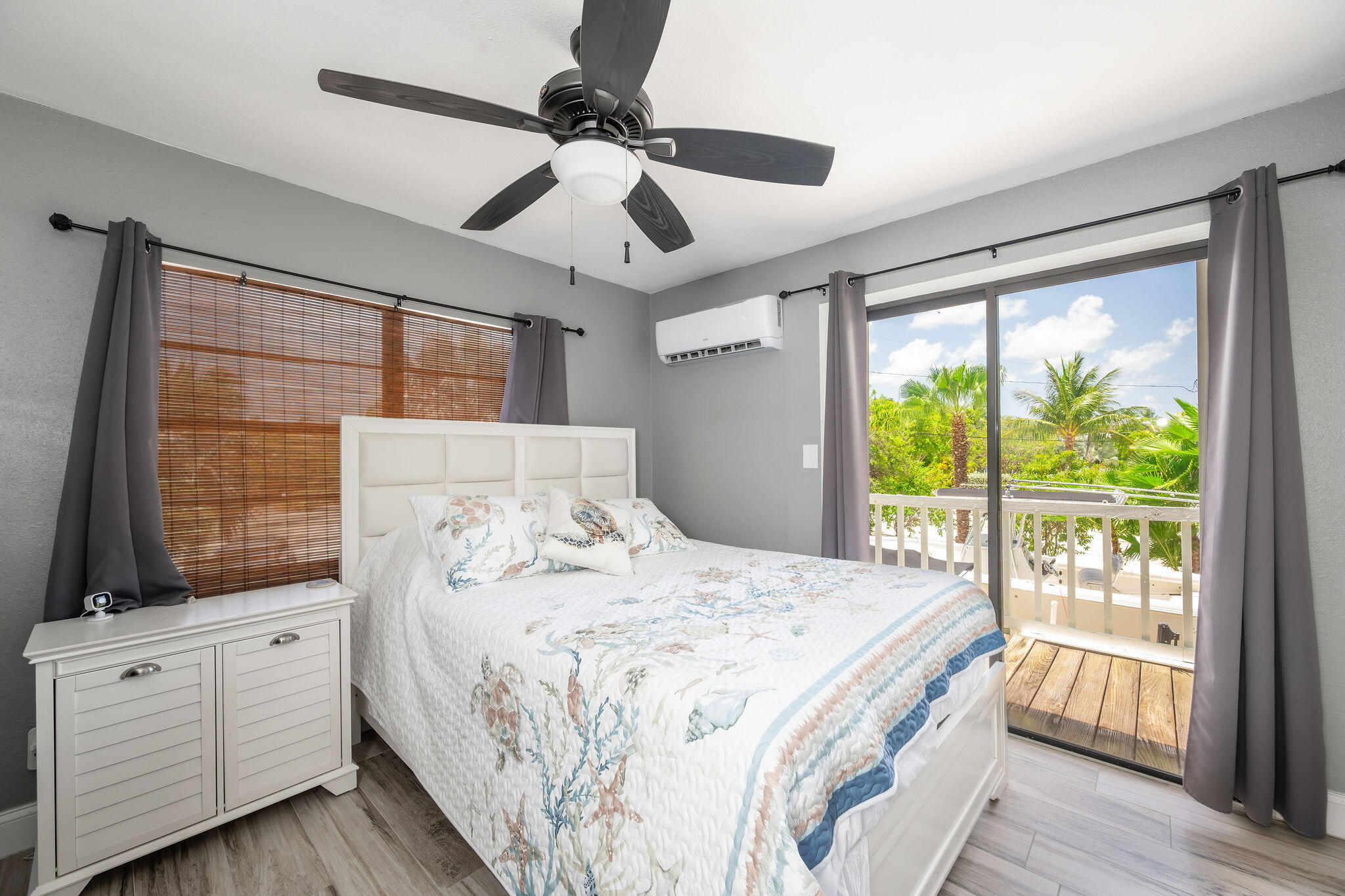 Bedroom with sea-life patterned bedding and sliding doors opening onto a palm-lined balcony.