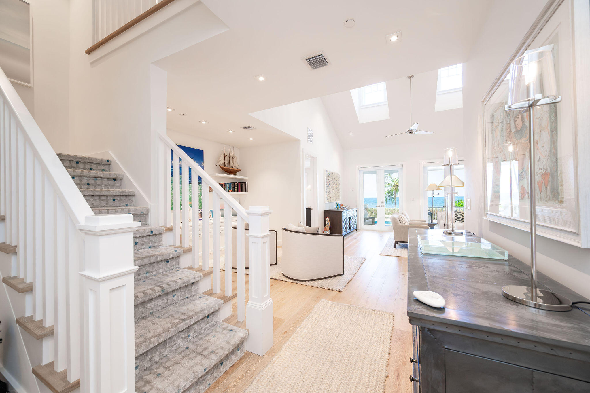 Bright living room with a carpeted staircase, skylights, and ocean views through glass doors.
