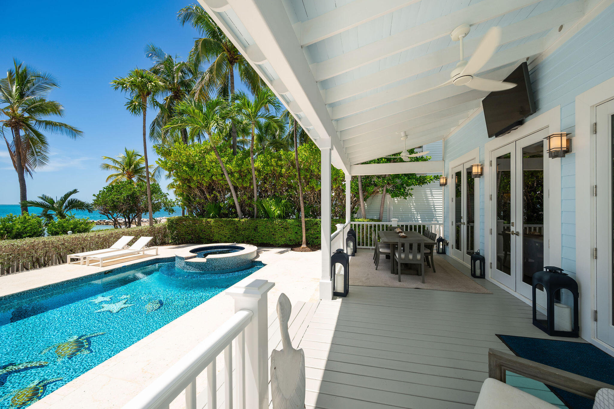 Swimming pool and raised spa beside a covered porch, with palm trees and ocean beyond.