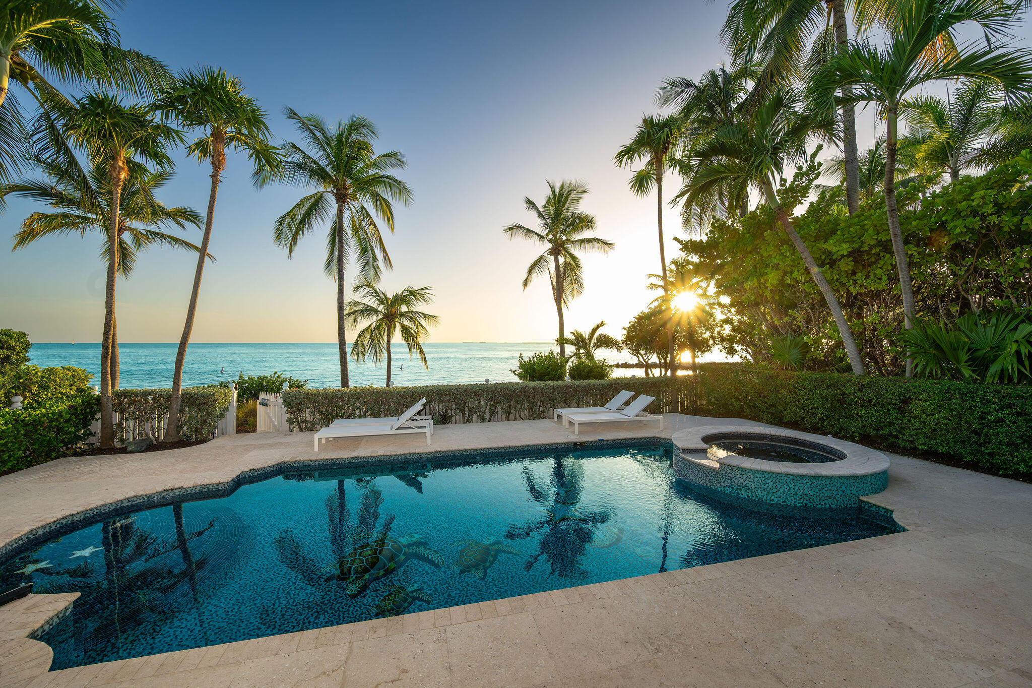 Oceanfront pool and spa framed by palm trees, with lounge chairs and the sunset over the water.