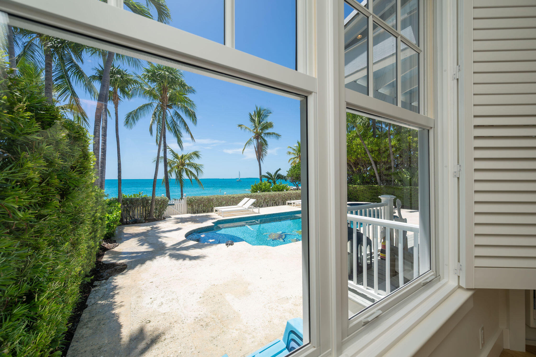Window view of a pool and palm trees beside the turquoise ocean.