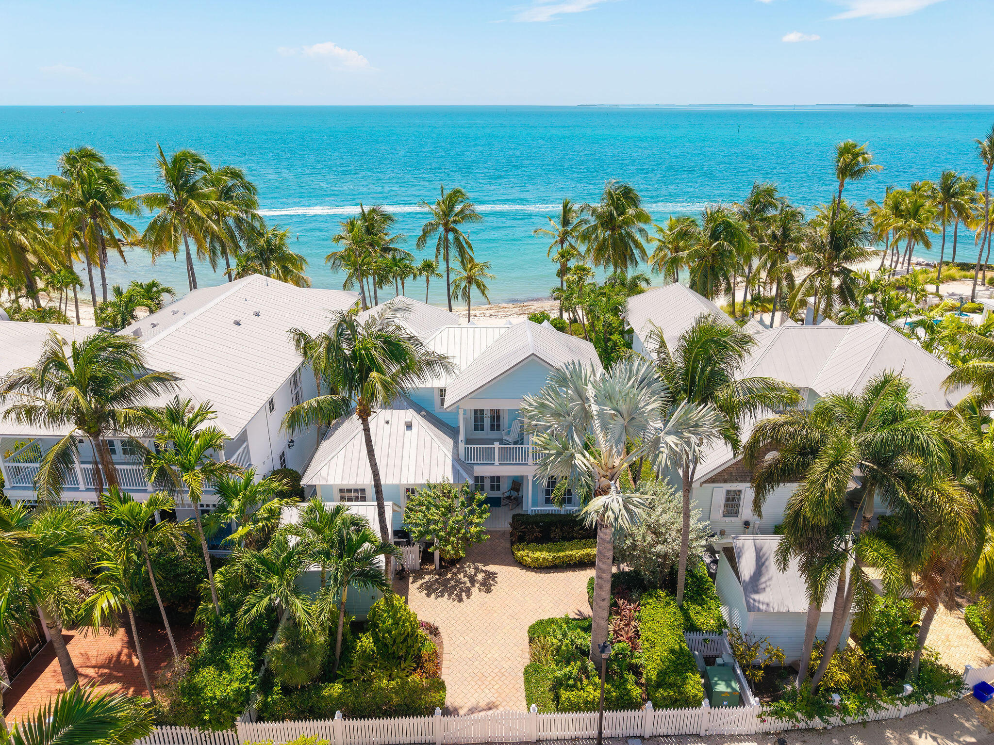 Aerial view of palm-lined beachfront homes with turquoise ocean beyond.