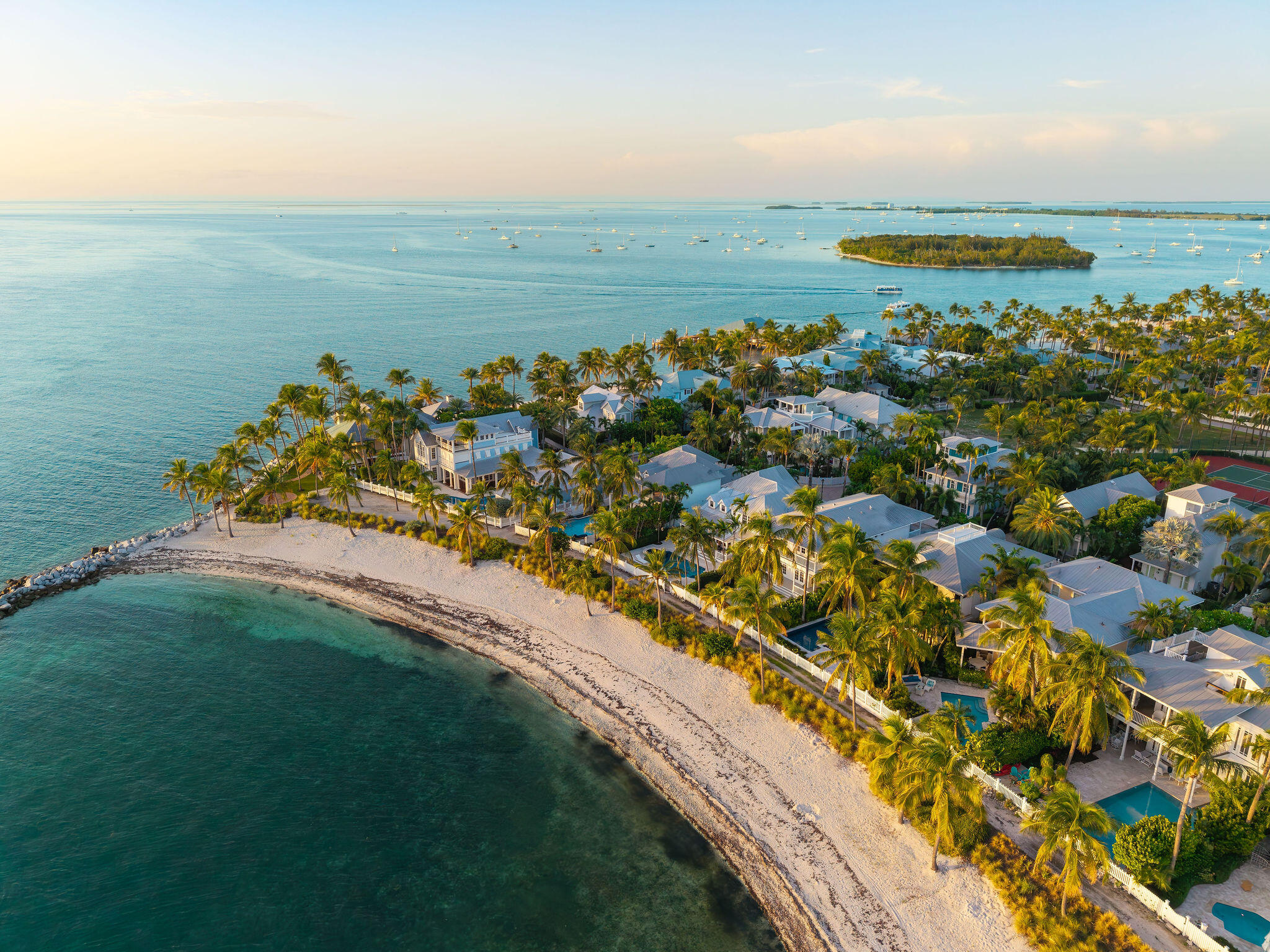 Aerial view of Sunset Key’s palm-lined homes, curved beach, and boats on the surrounding water.