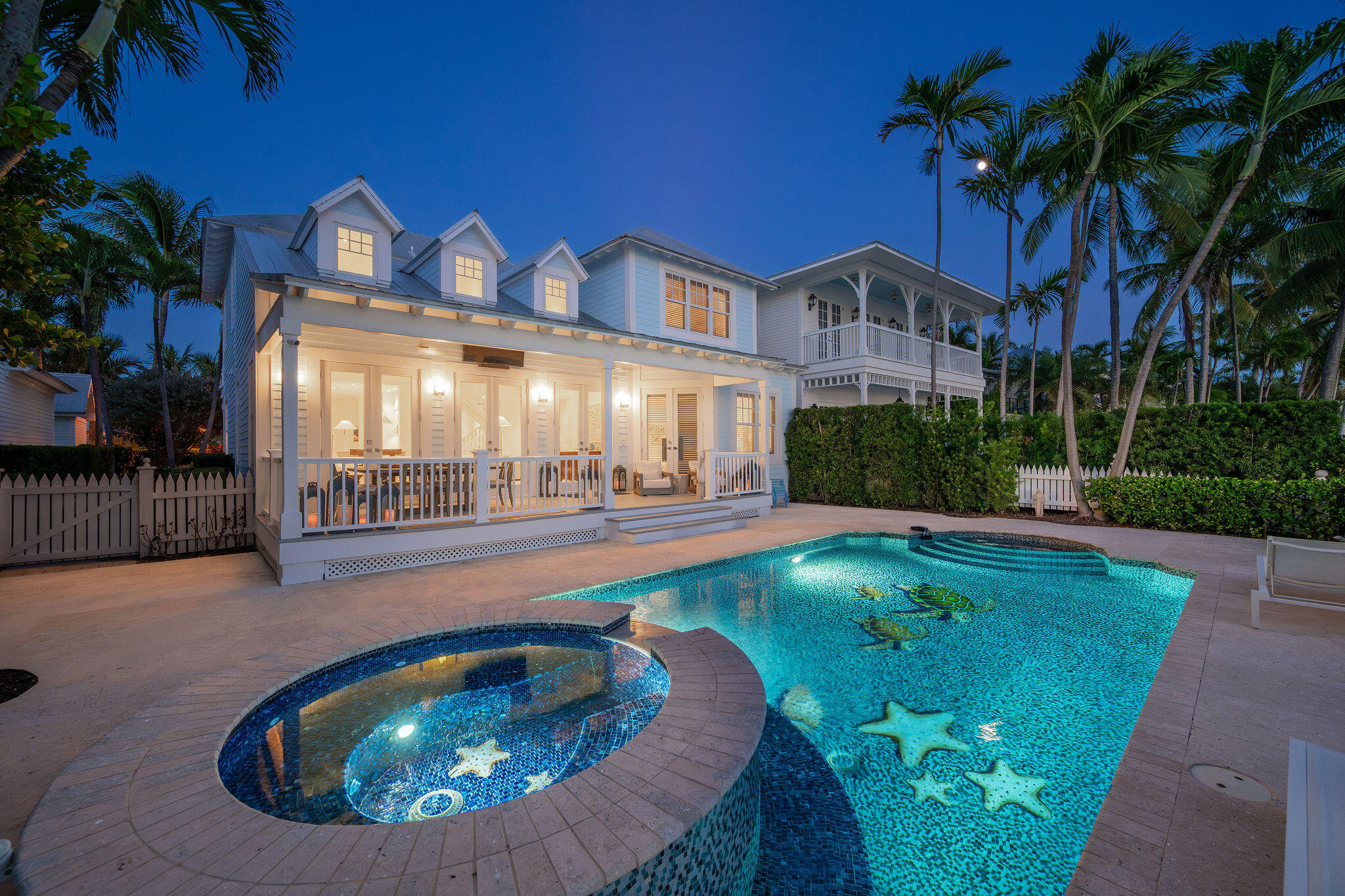 White coastal home with an illuminated pool and circular raised spa at dusk.