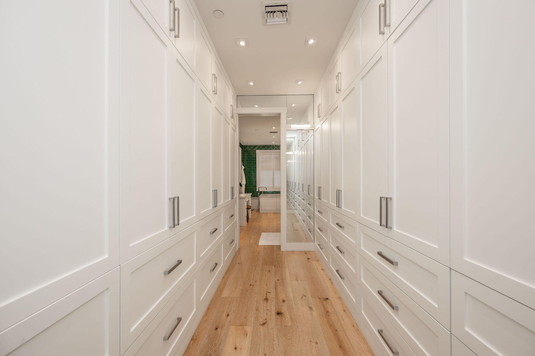 Walk-in closet with white built-in cabinets, wood flooring, and a full-length mirror.