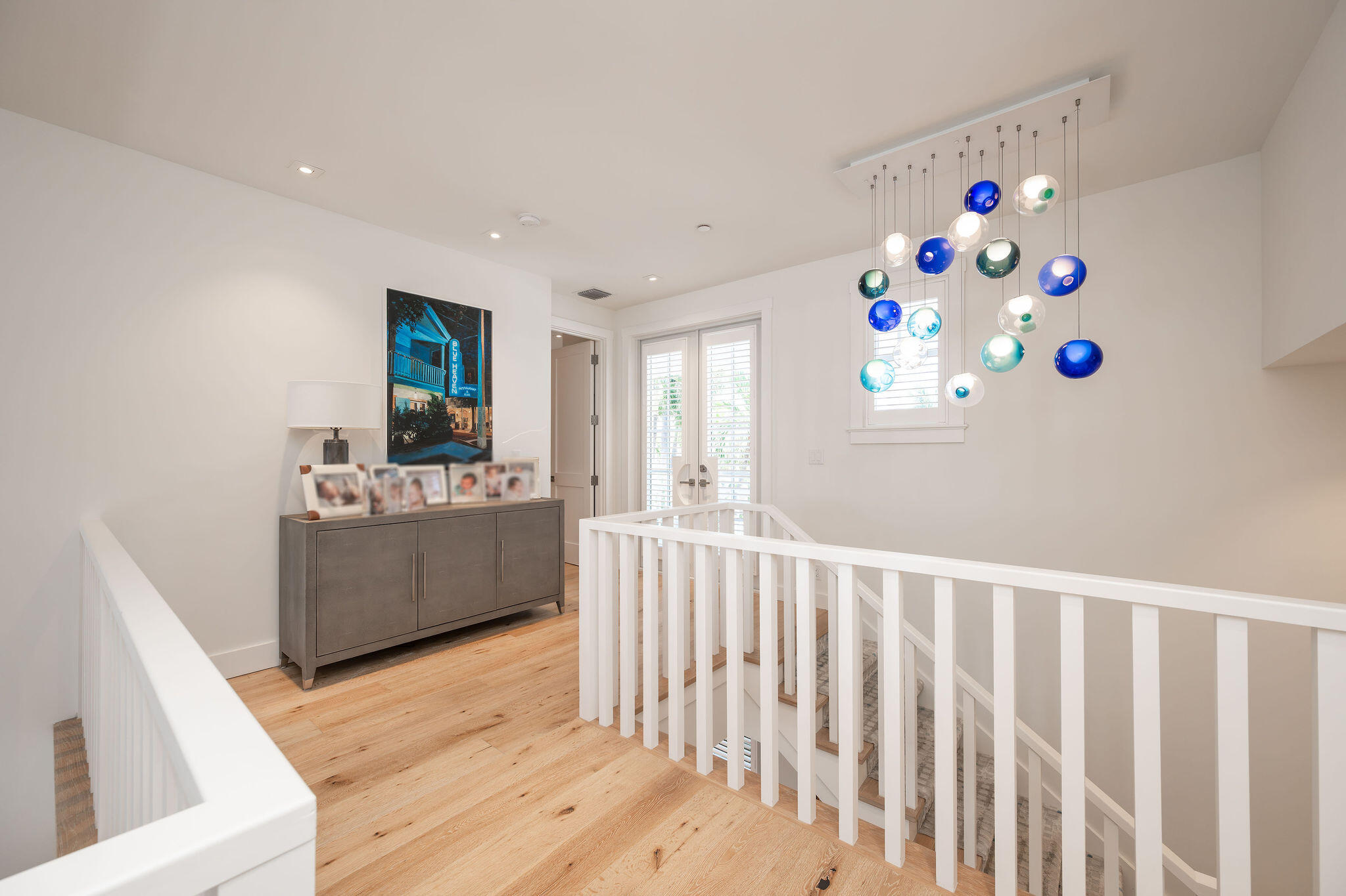 Upstairs landing with white stair railings, a gray console, and a sculptural blue-and-white pendant chandelier.